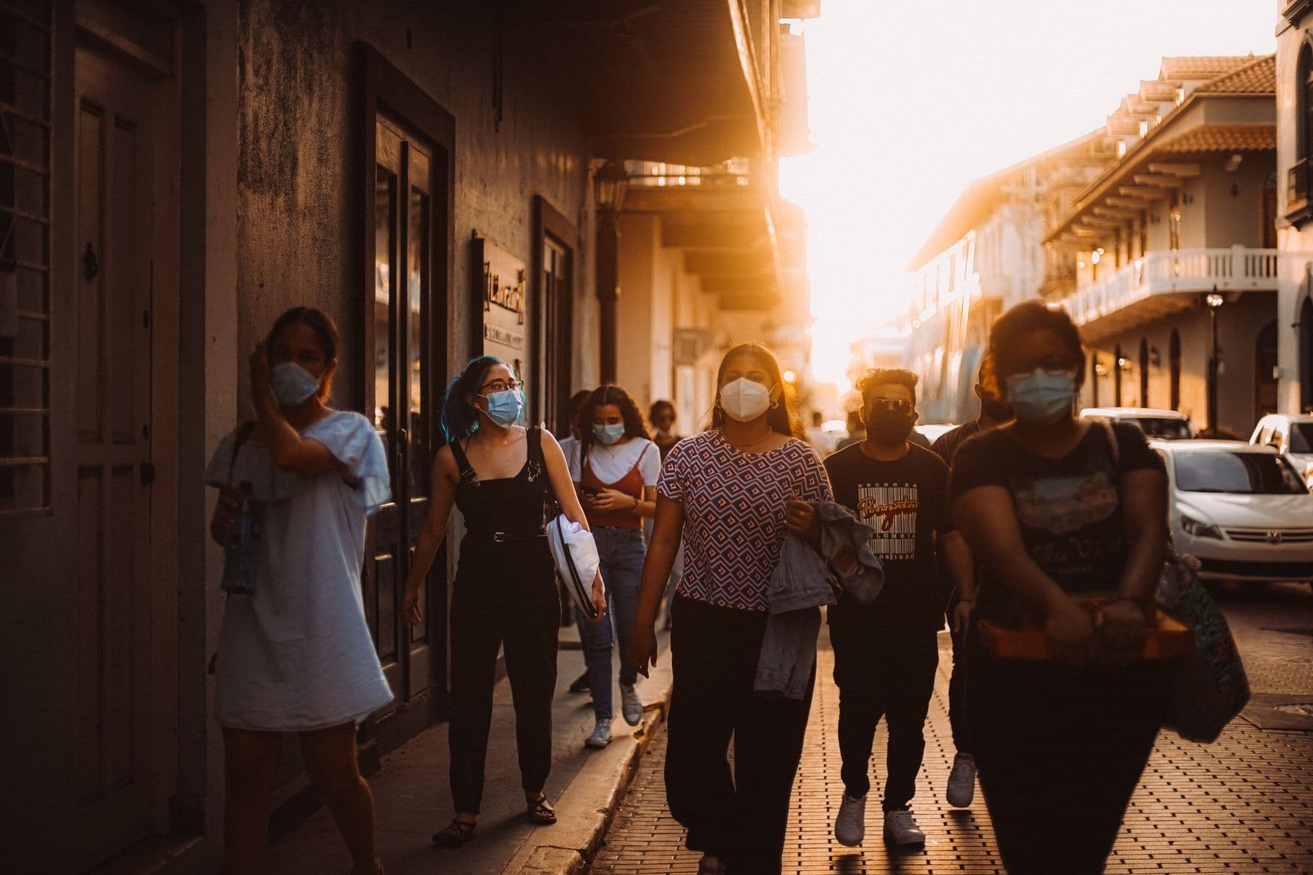 A group of people wearing face masks walks outdoors during sunset, reflecting pandemic precautions.