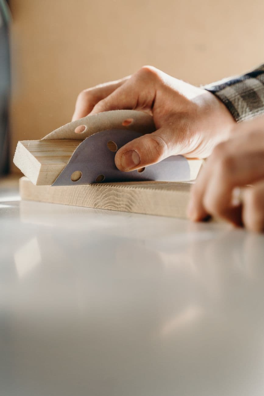 Hands sanding a wooden block, showcasing carpentry craftsmanship and attention to detail.