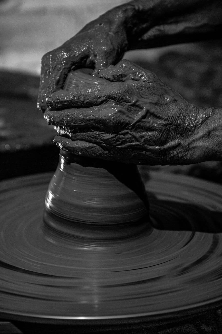 Black and white close-up of skilled hands shaping clay on a pottery wheel.