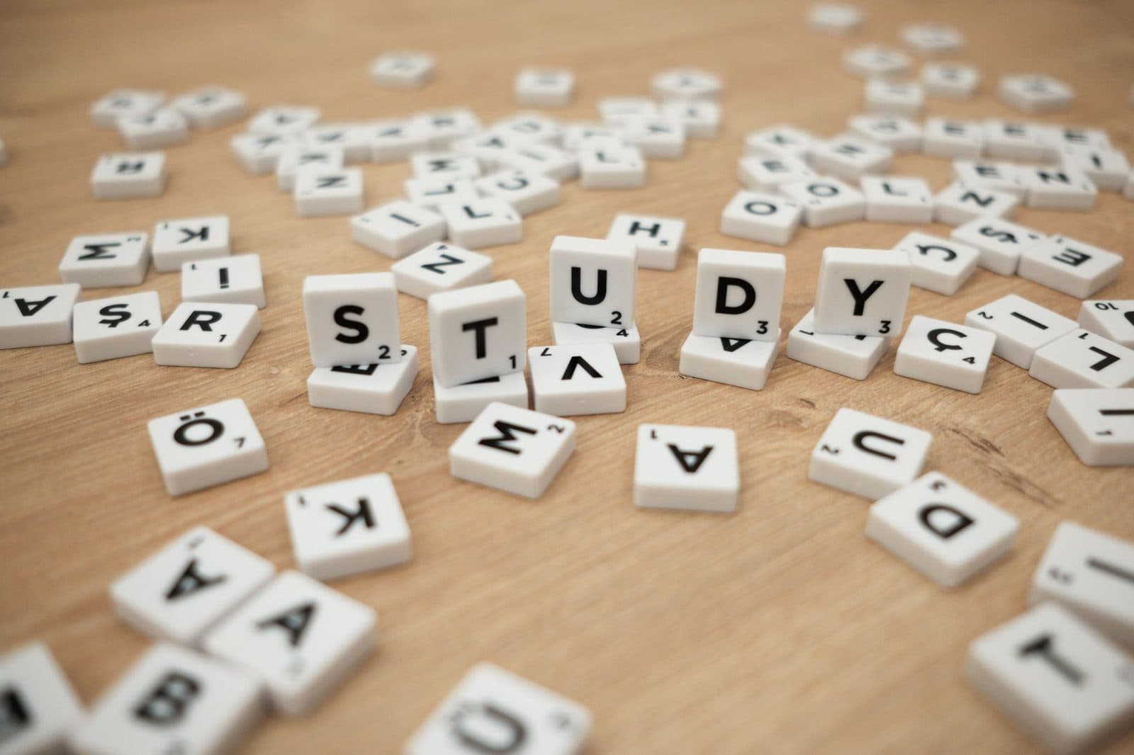 Close-up of letter tiles spelling 'Study' amidst scattered letters on a wooden surface.