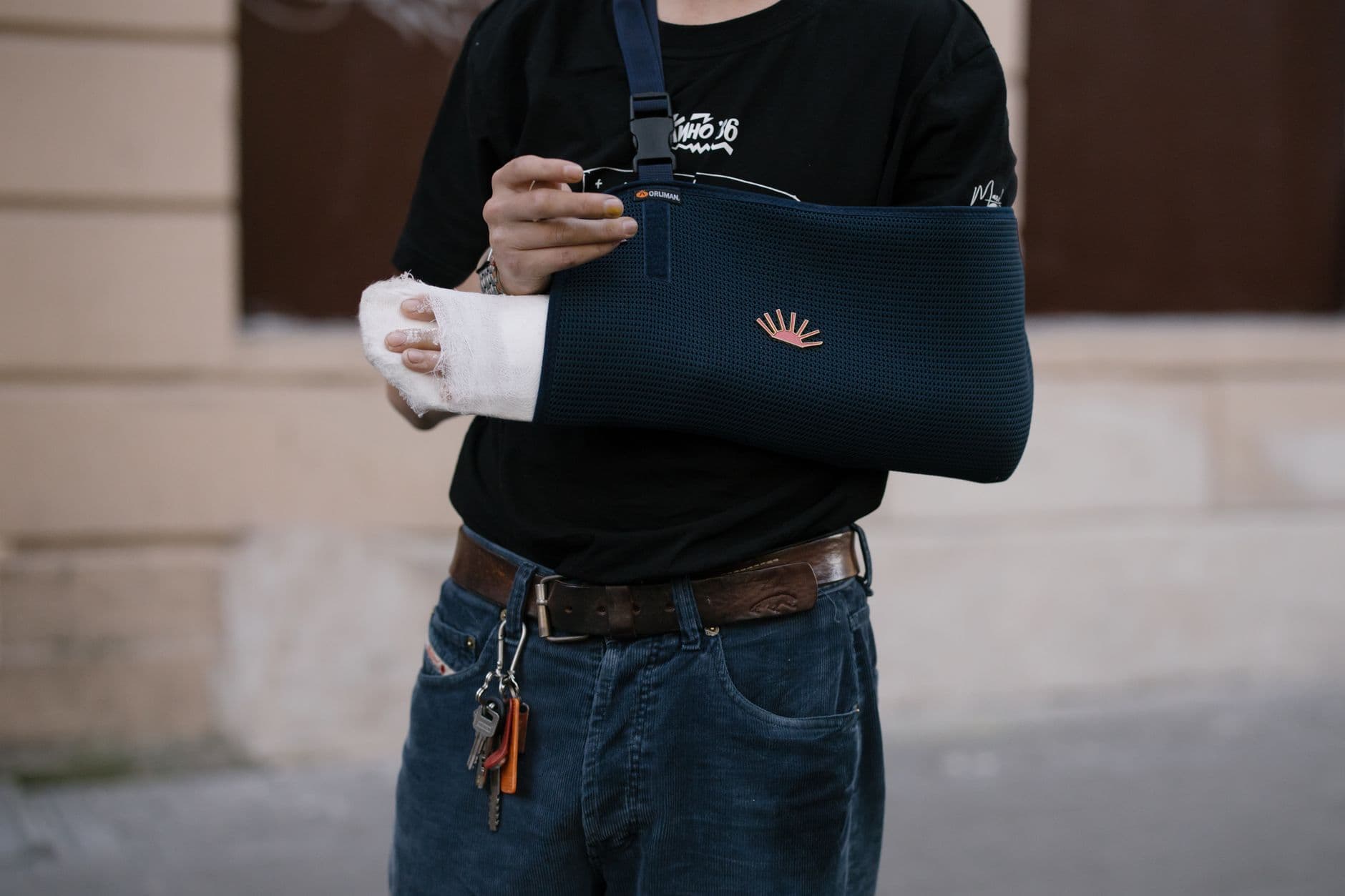 A man wearing a dark sling with a bandaged arm, standing outdoors in casual attire.
