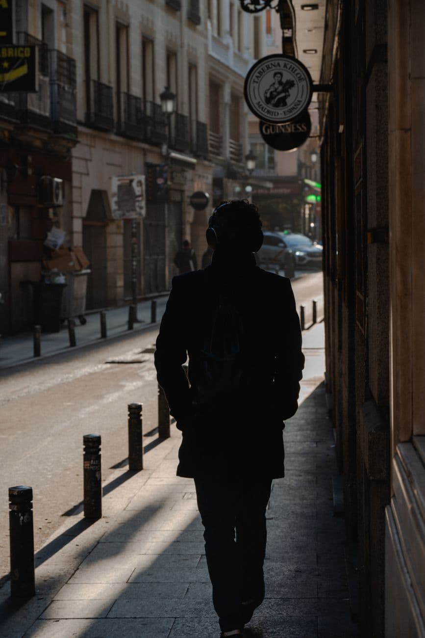 Backlit silhouette of a person walking on a narrow street in Madrid, Spain during daylight.