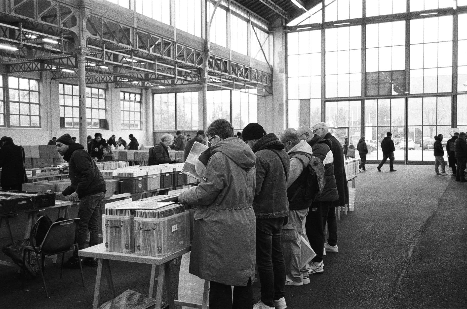 Crowded indoor market in Nancy, France with people browsing stalls in black and white.