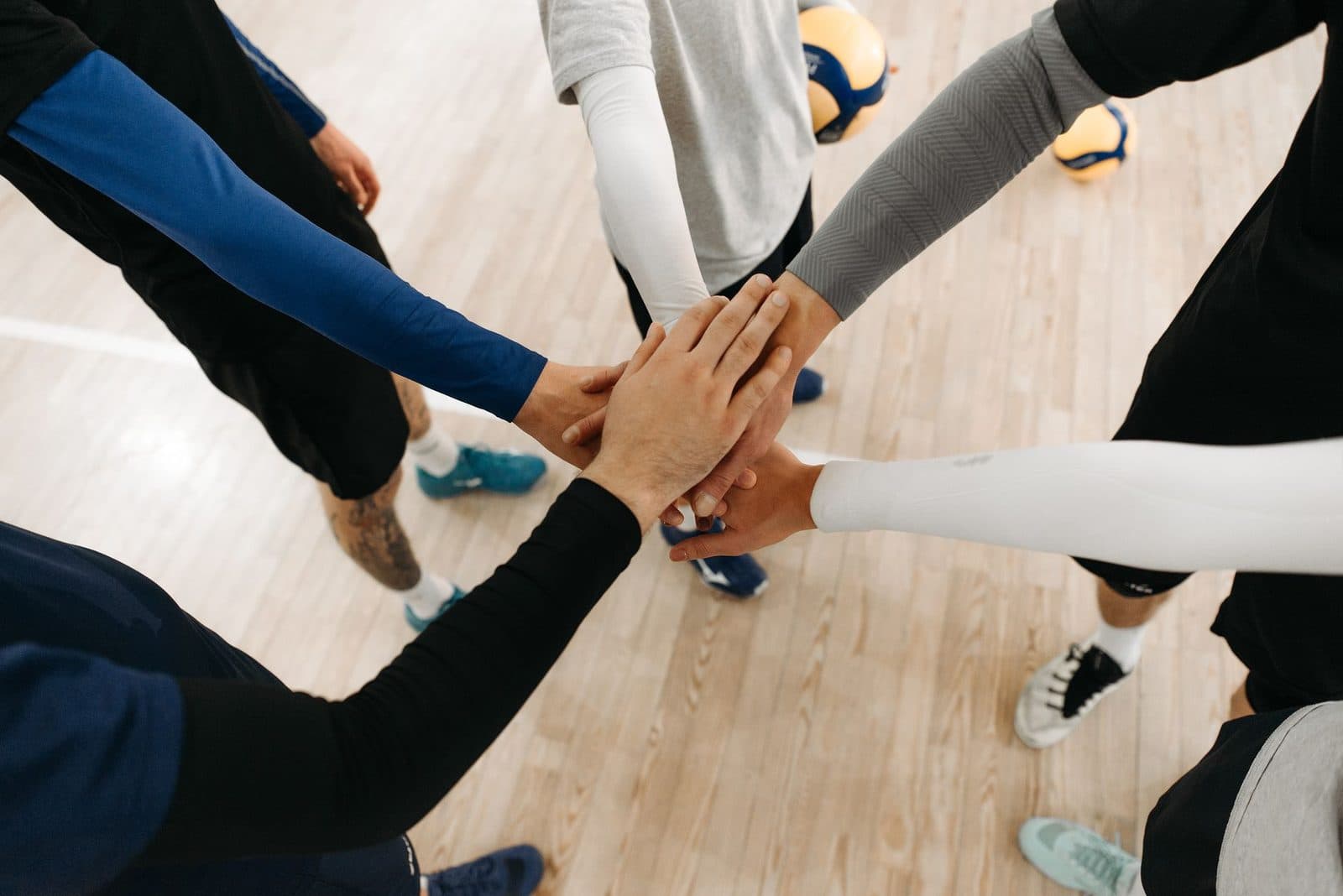 Close-up of athletes joining hands in a motivational sports huddle on an indoor court.