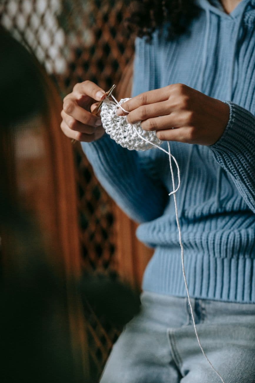 A person skillfully crocheting a piece of fabric, showcasing a handmade craft indoors.
