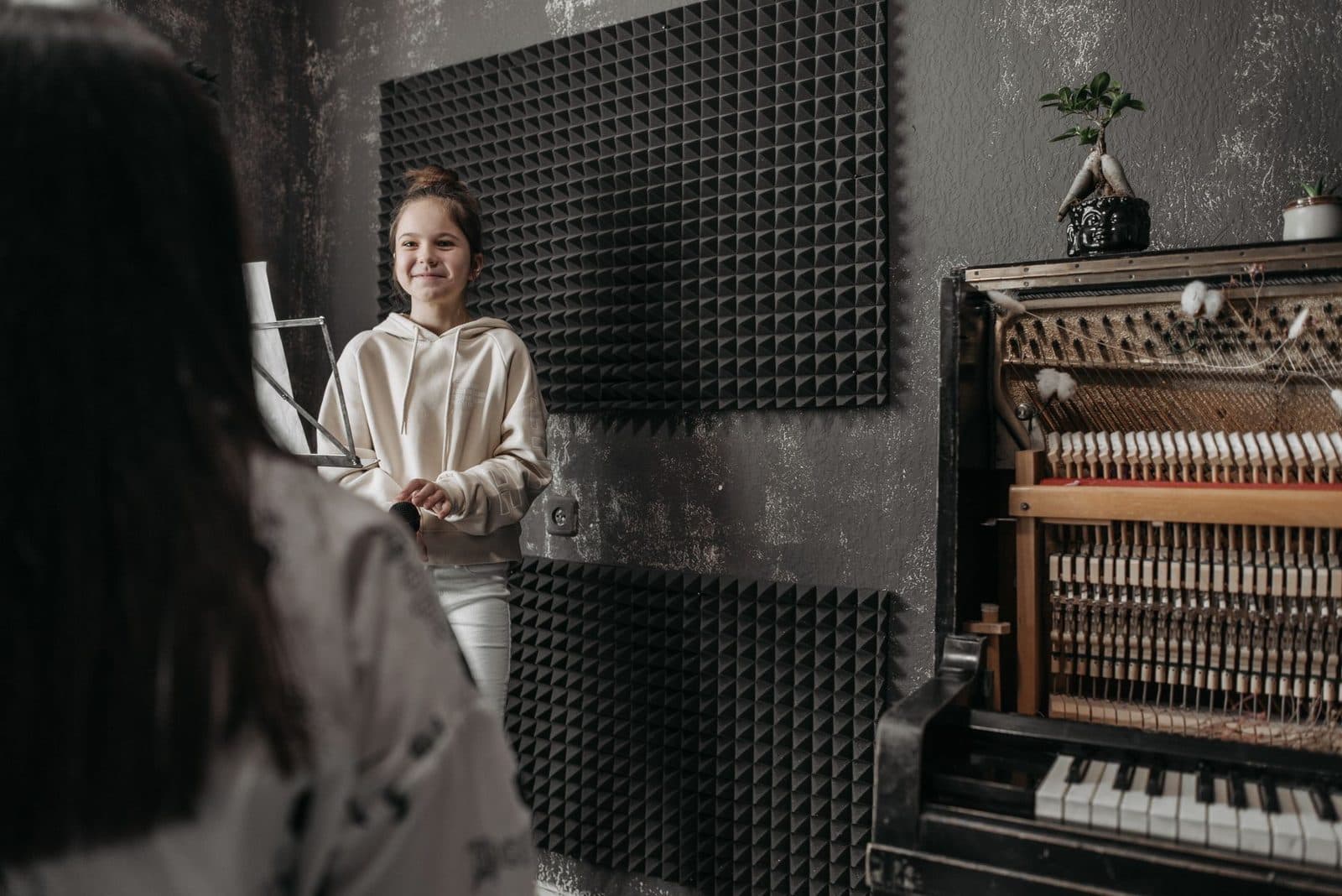 A young girl smiling during a music lesson in a studio with an open piano.