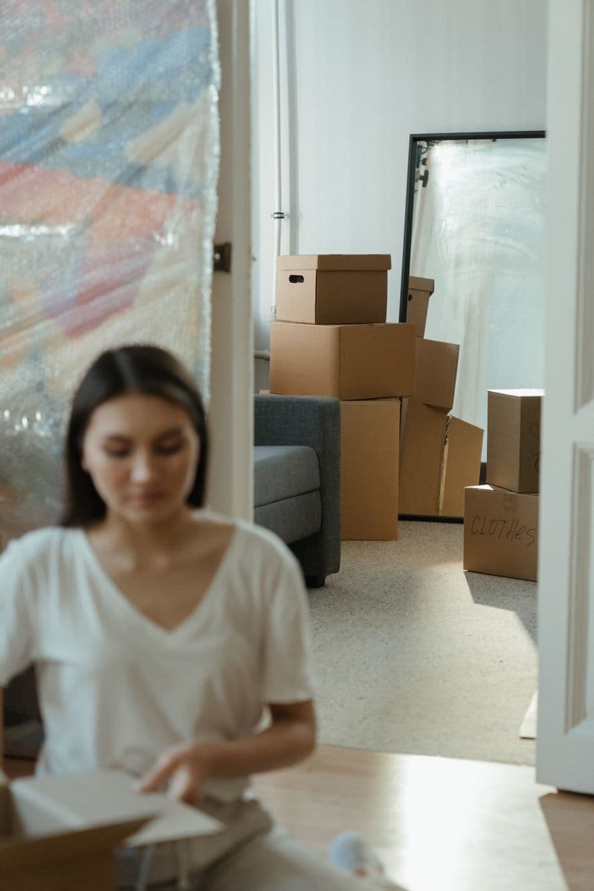 A woman sits and unpacks moving boxes in a bright, modern apartment.