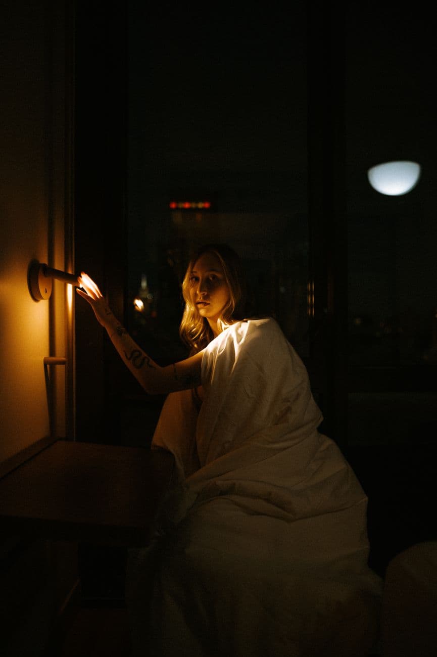 Moody portrait of a woman by a lamp in a New York city room at night.