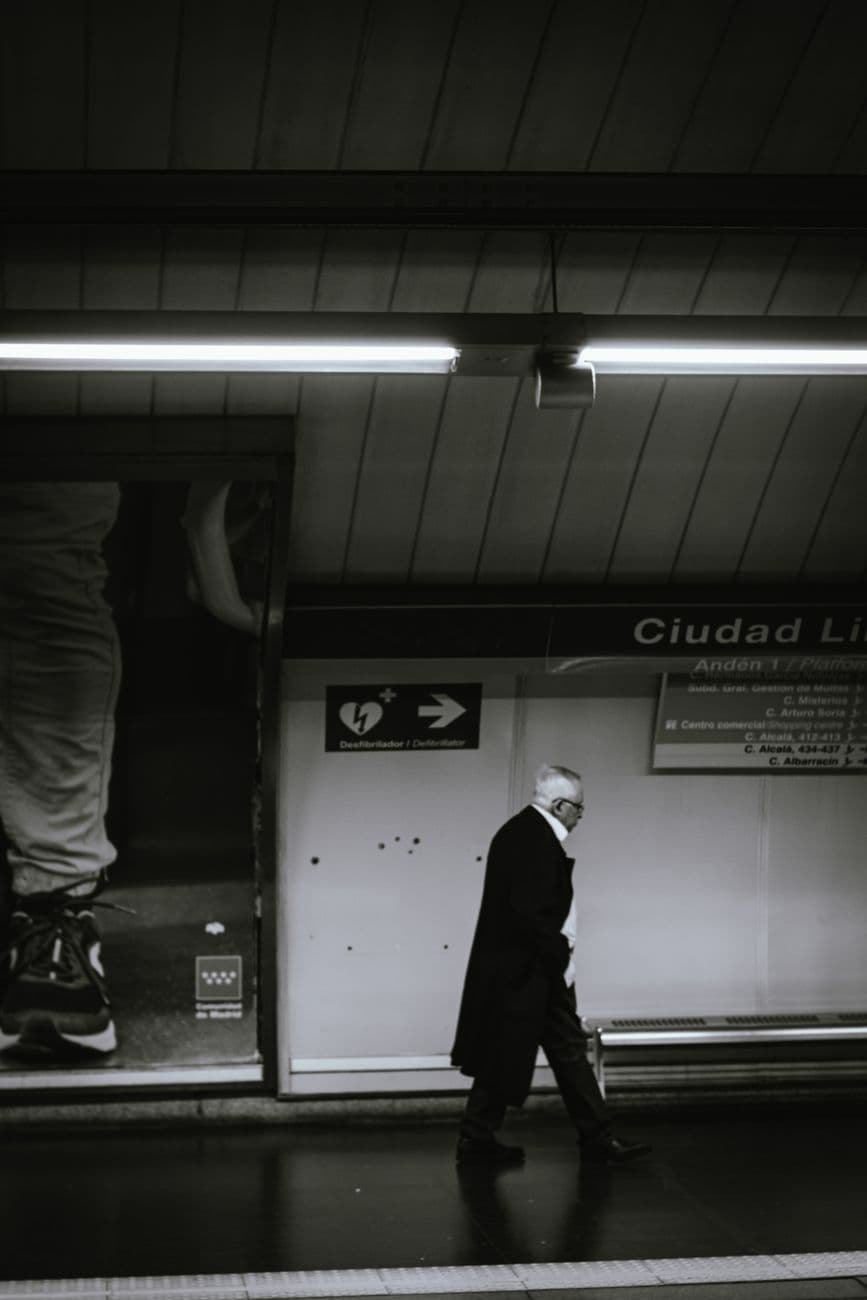 Black and white photo of an elderly man walking in Ciudad Lineal subway station, Madrid.