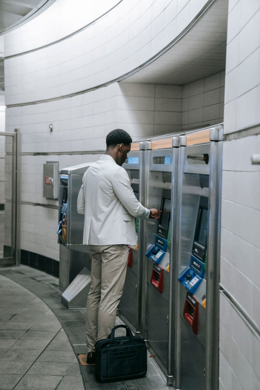 A man purchases a ticket from a machine at a train station, wearing business attire.
