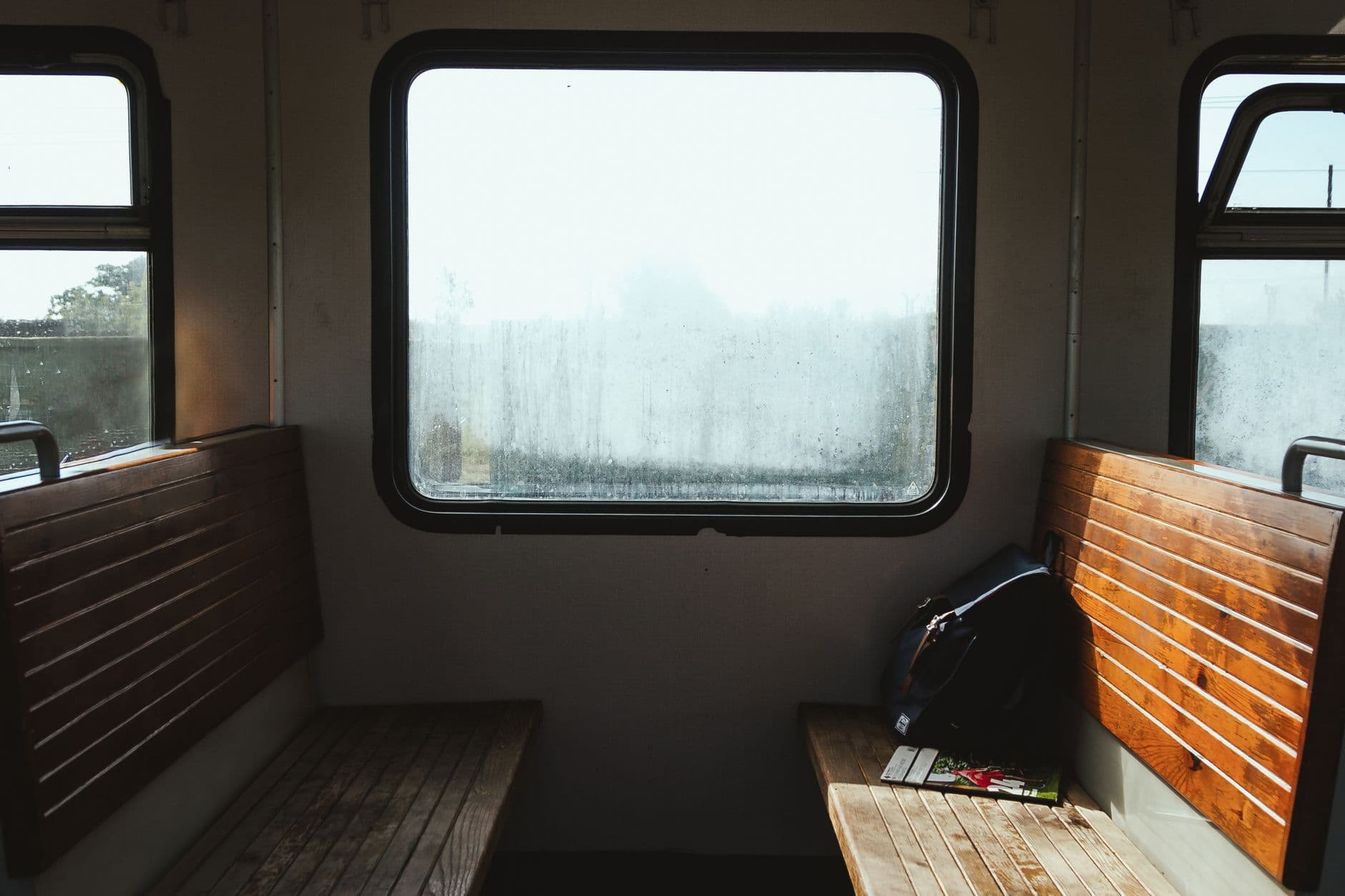 Old empty benches with backpack and magazine near shiny window in train in sunlight