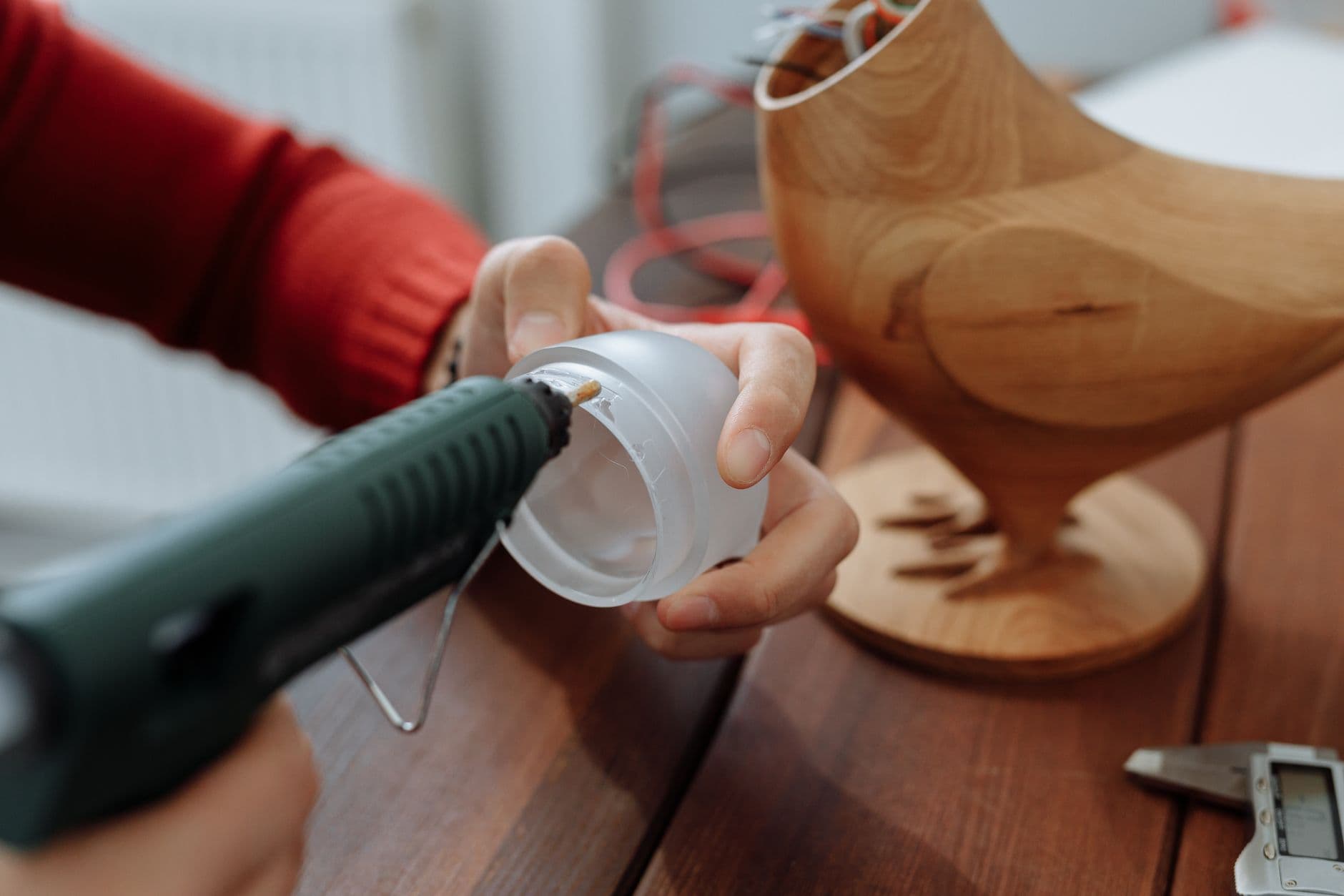 Close-up of a person gluing a plastic lid next to a wooden chicken model on a table.