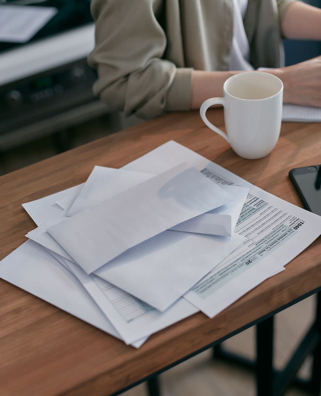 A casual workspace with envelopes, tax documents, and a coffee cup on a wooden table.