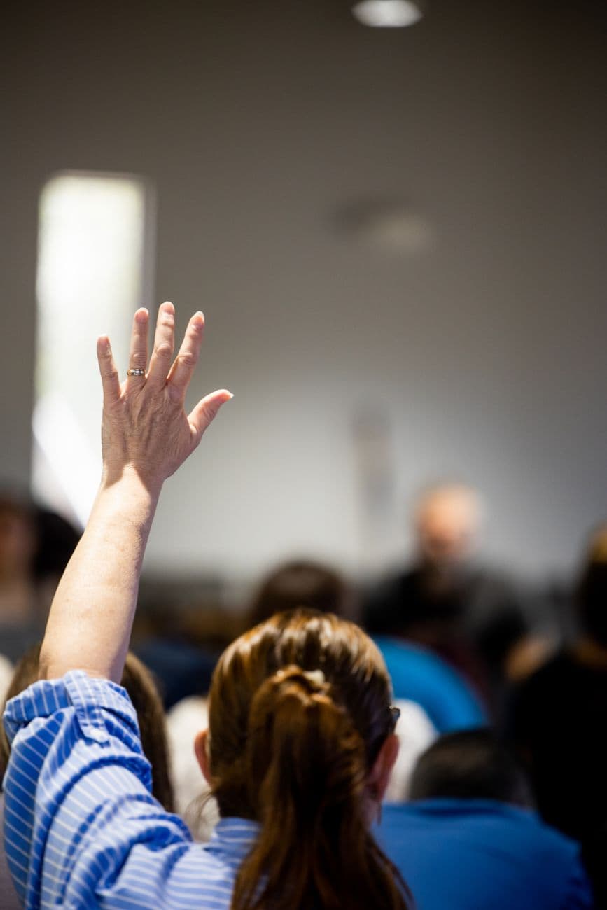 A person raises their hand during an indoor event, indicating participation or inquiry.