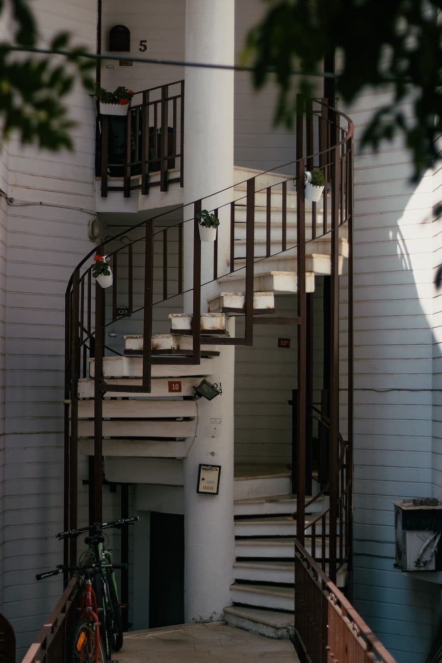 Stylish spiral staircase with hanging plants in a modern apartment complex, offering a unique architectural view.