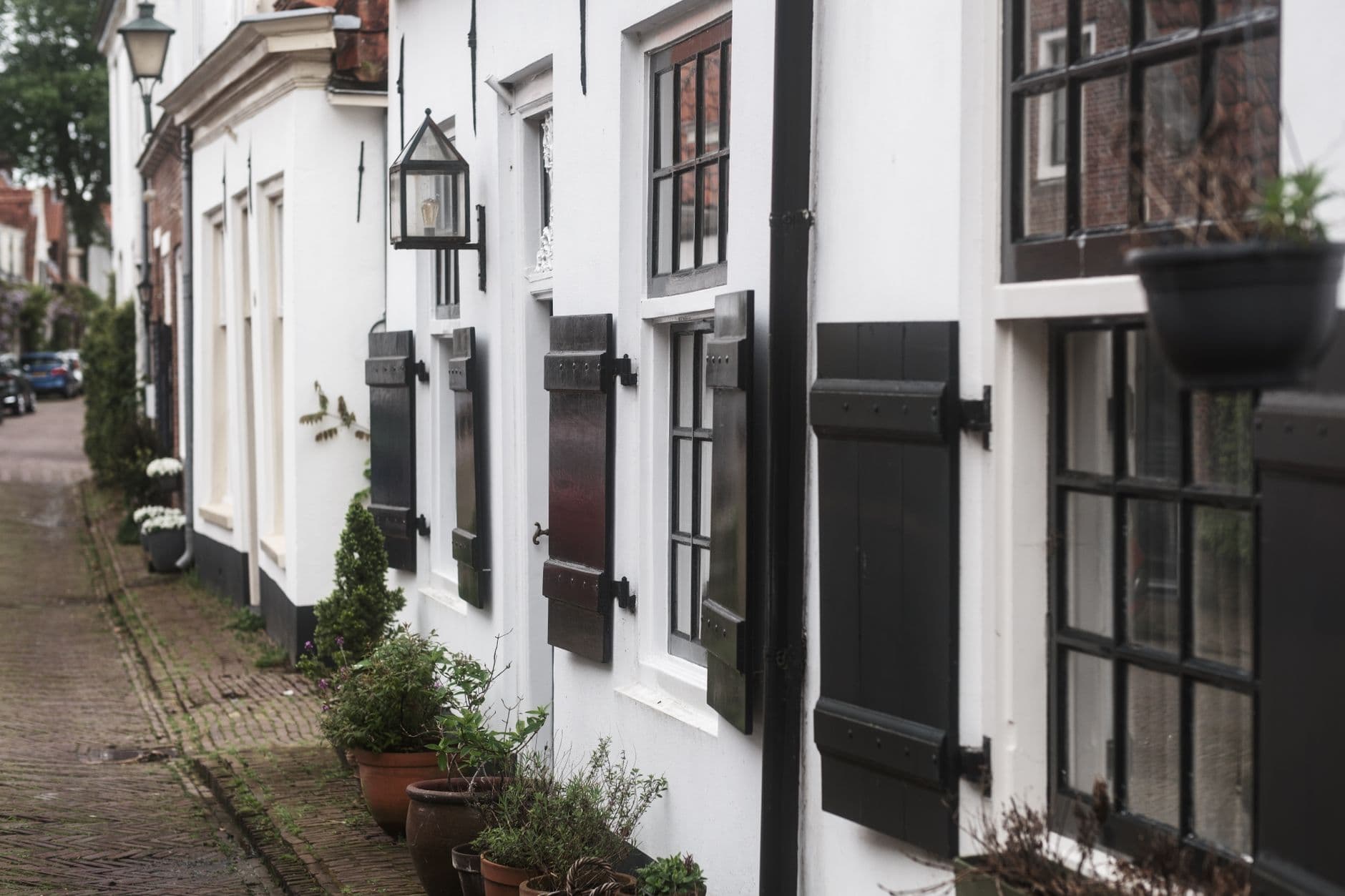 Picturesque street with white houses, black shutters, flowerpots, and traditional lamps.