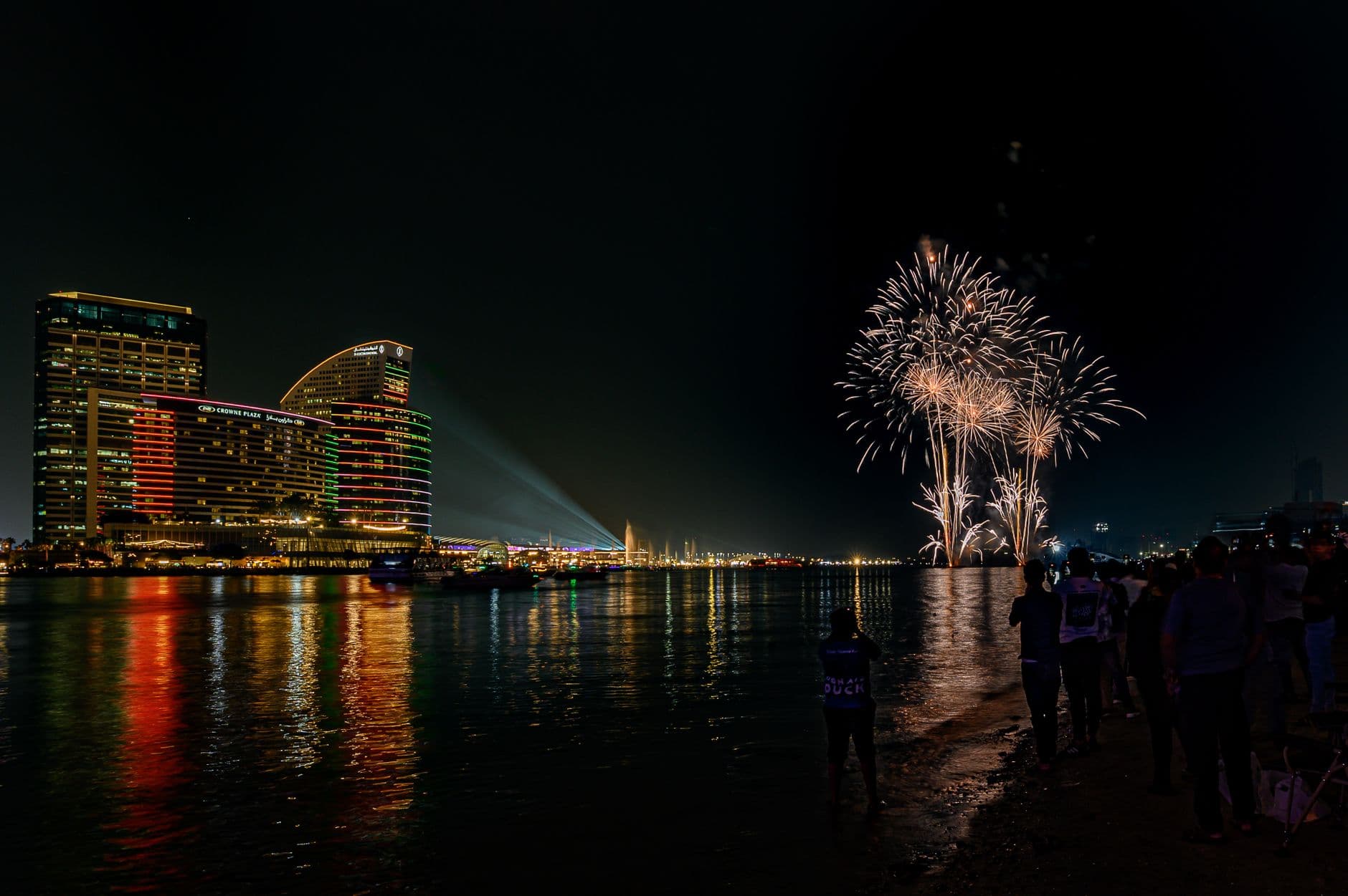 Spectacular fireworks display illuminating city waterfront at night, reflecting vivid lights.