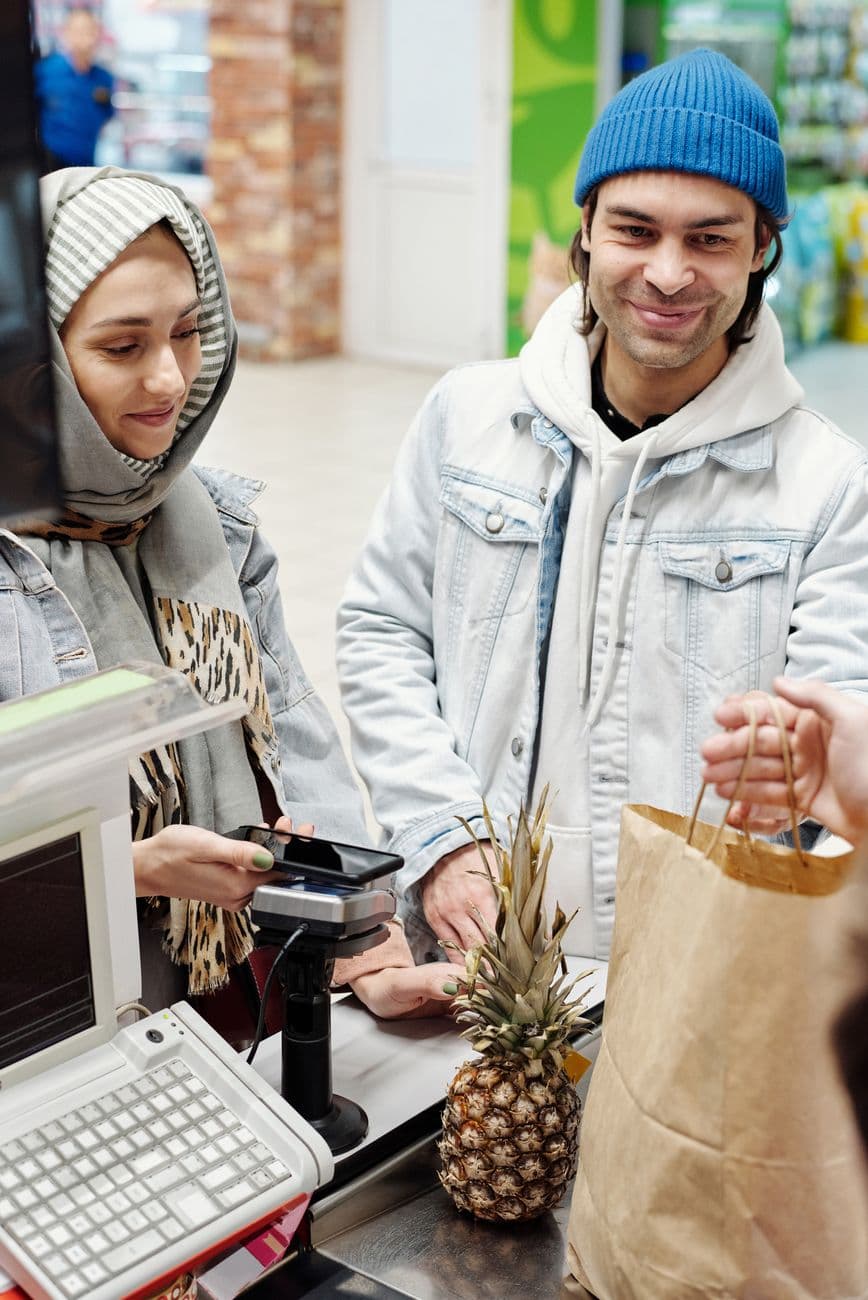 A smiling couple using a smartphone to pay at a supermarket checkout counter.