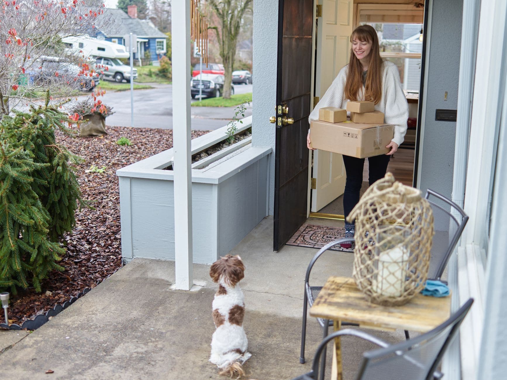 Smiling woman receives packages at her door, watched by a small dog.