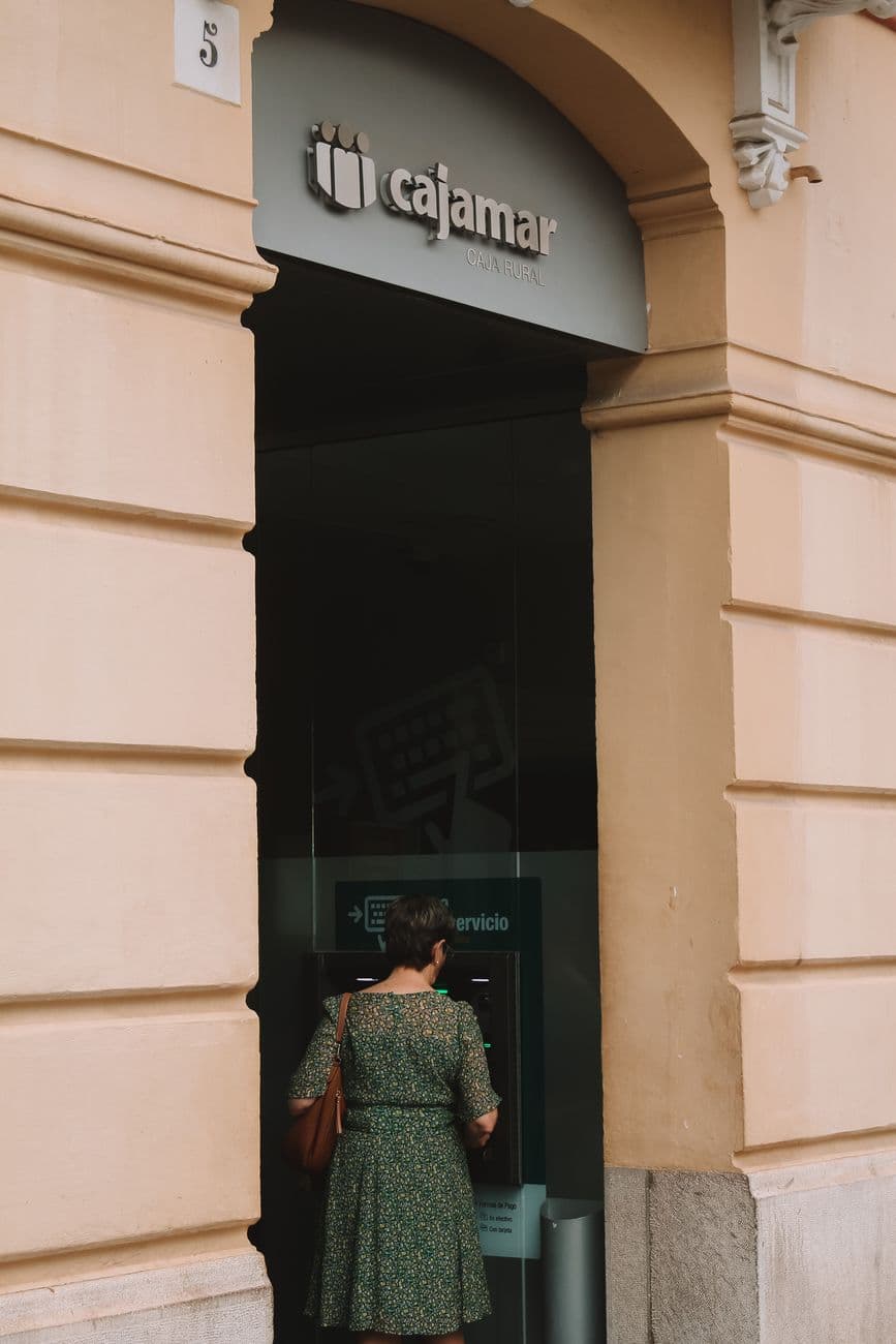 Woman at ATM outside Cajamar bank. Urban setting, daytime transaction.