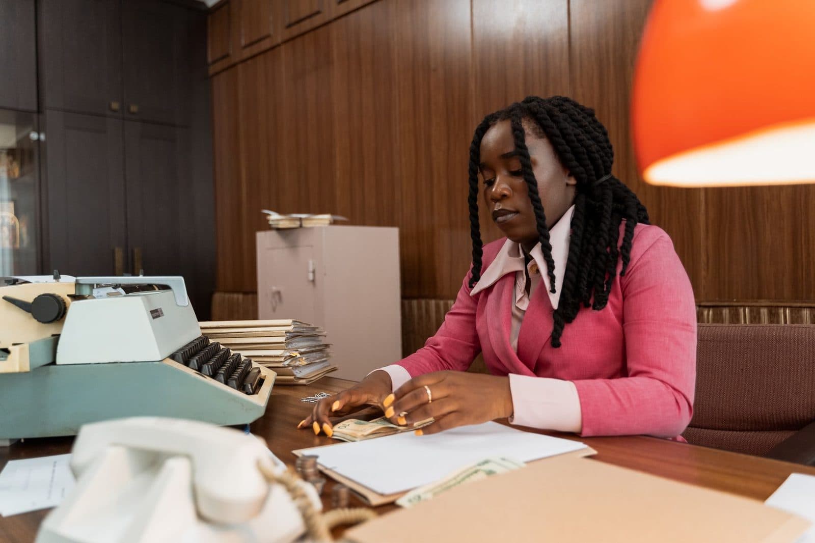 African American woman in business attire counting money at a vintage office desk.