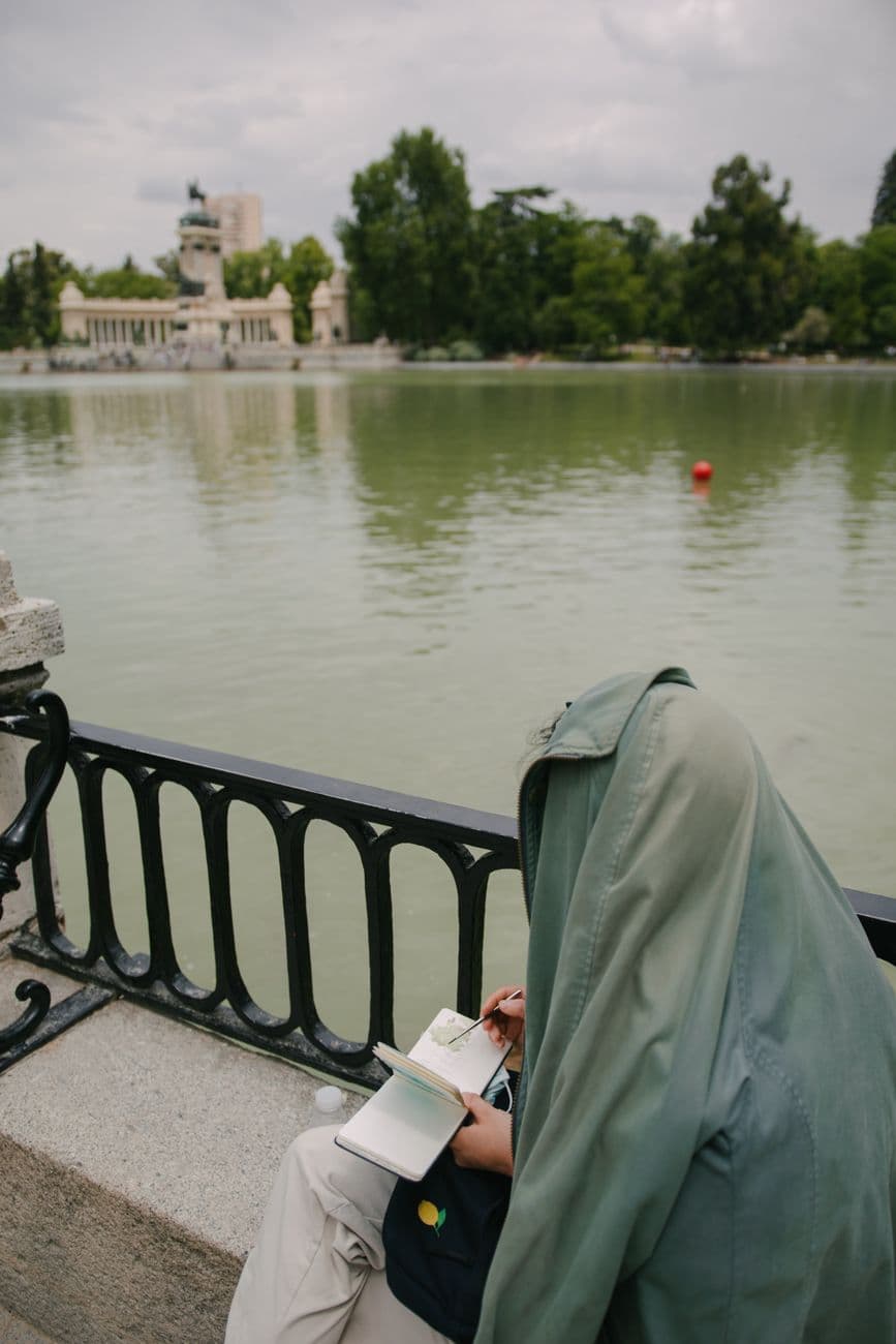 Adult sketching in a park by the lake in Madrid, capturing urban tranquility.