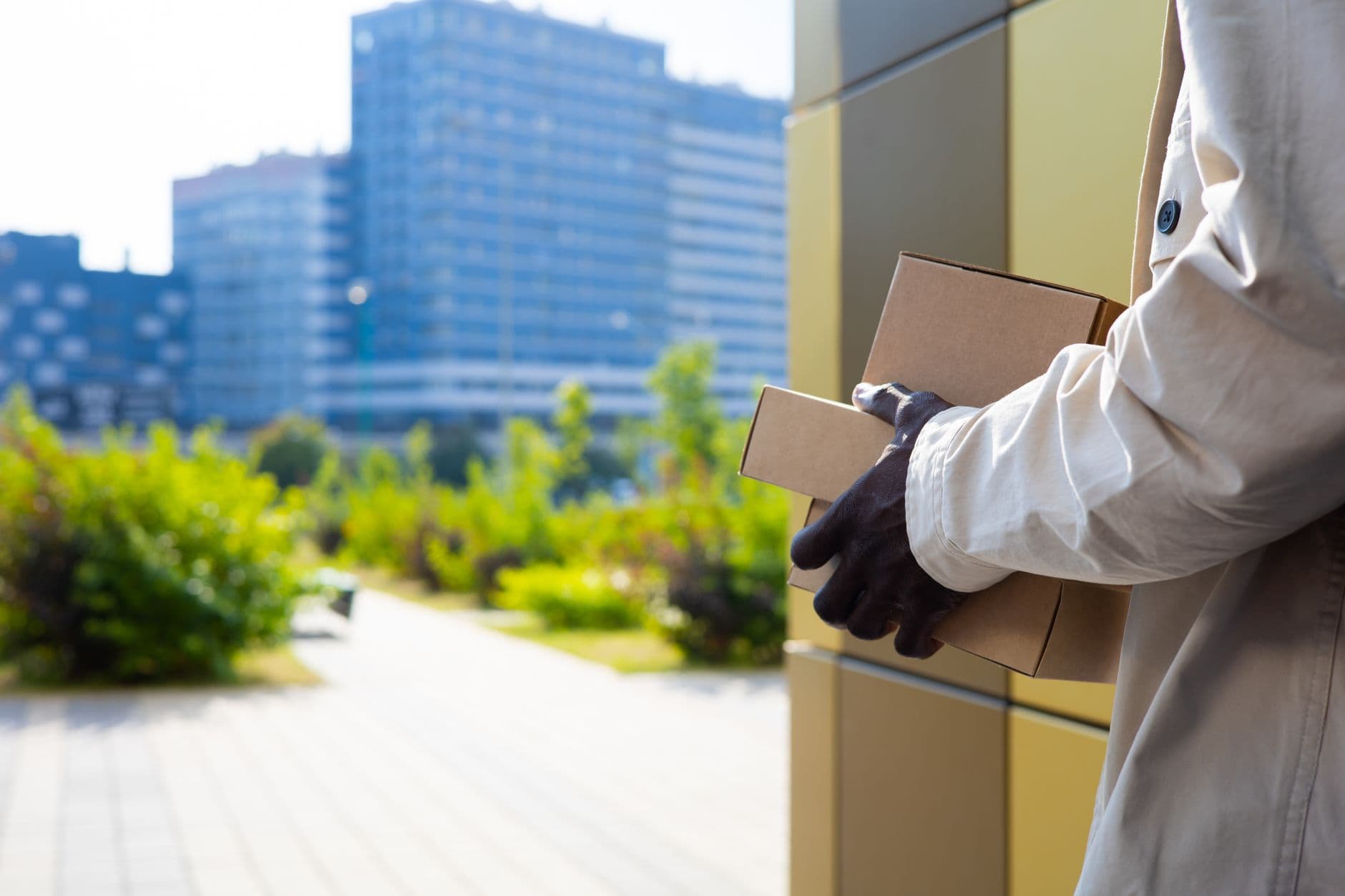 A delivery person carrying parcels in an urban setting with modern buildings.