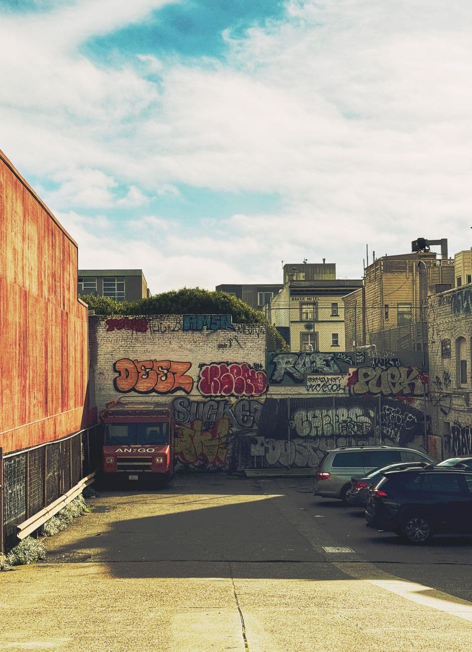 Colorful graffiti on urban alley walls with parked cars, sunny day.
