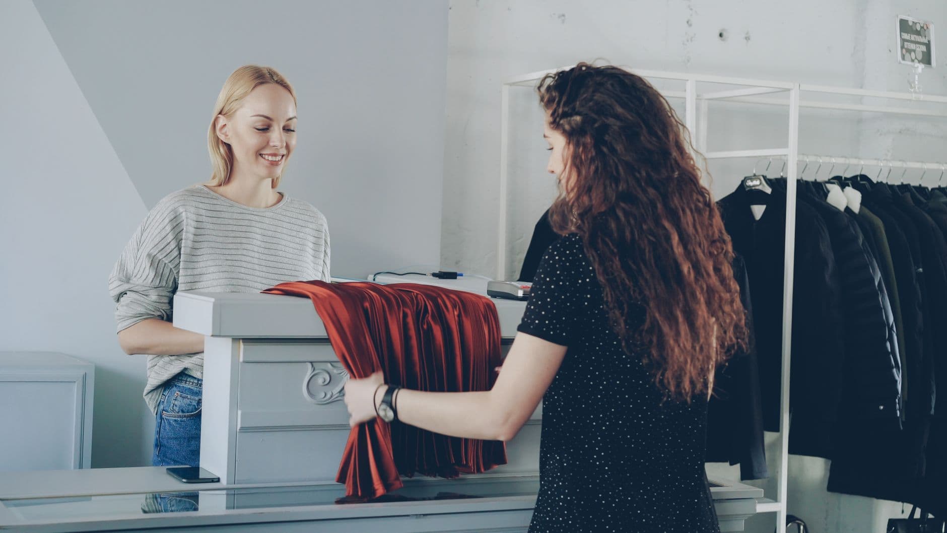 Friendly retail interaction between two women at a clothing store counter.