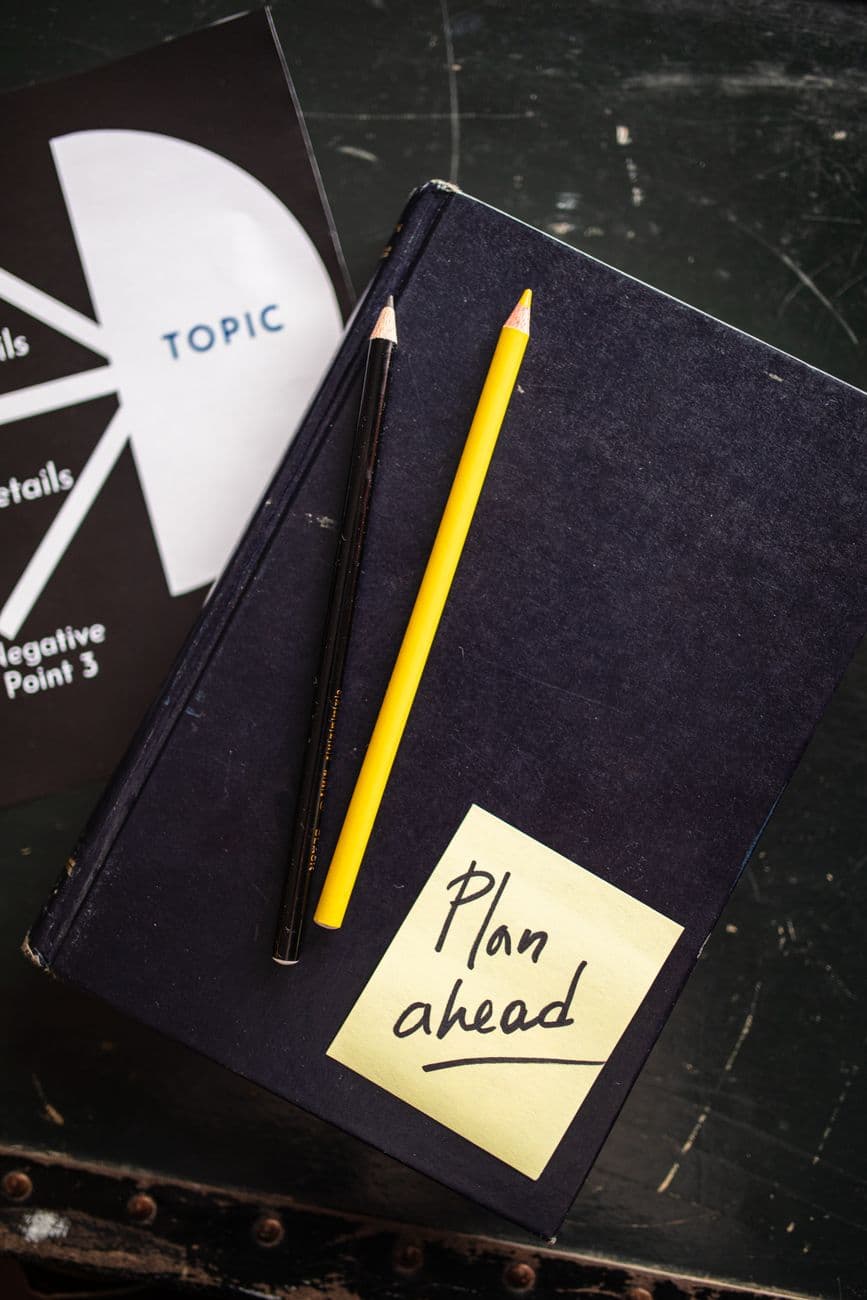 Top view of a book with pencils and a 'Plan ahead' note on it for organization.