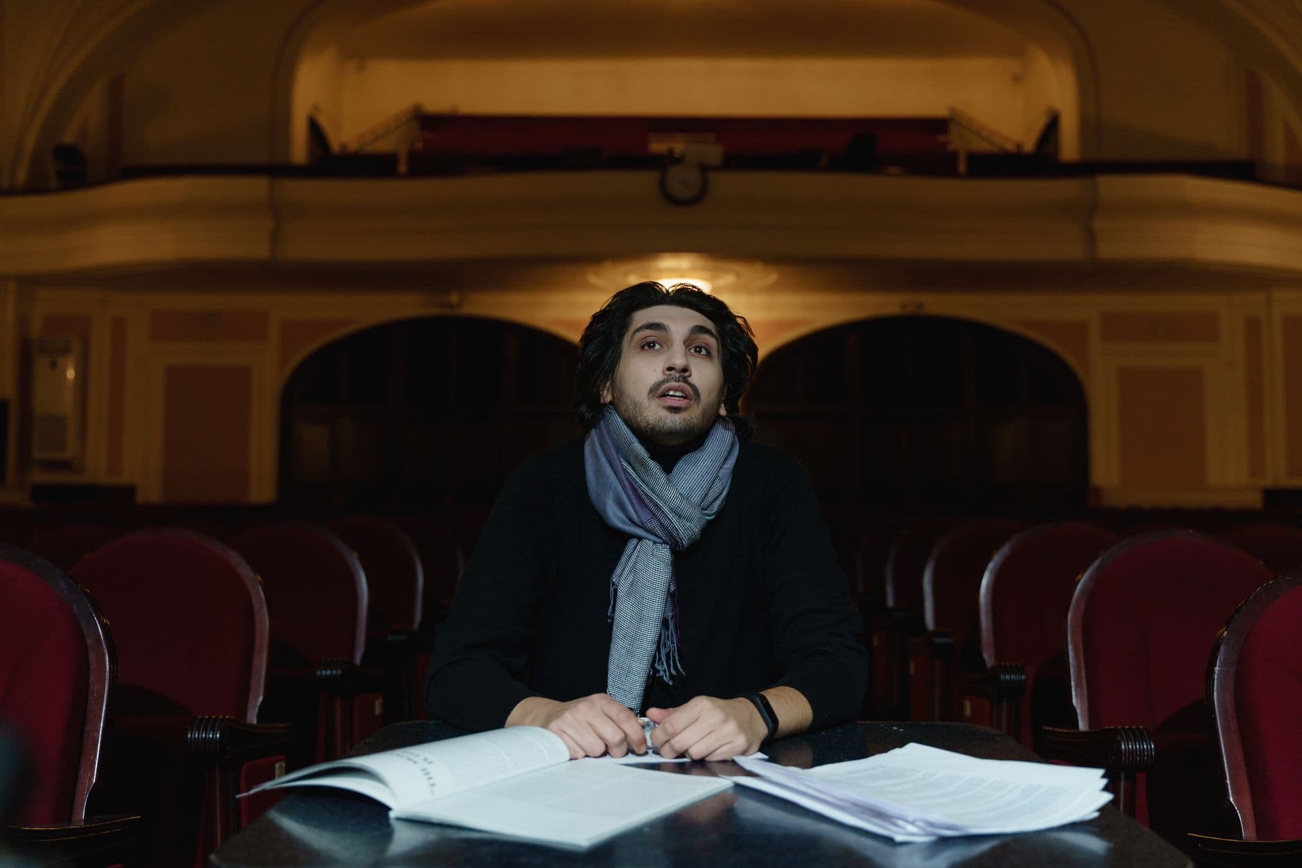 A theatre director rehearses with a script in a cozy auditorium setting.