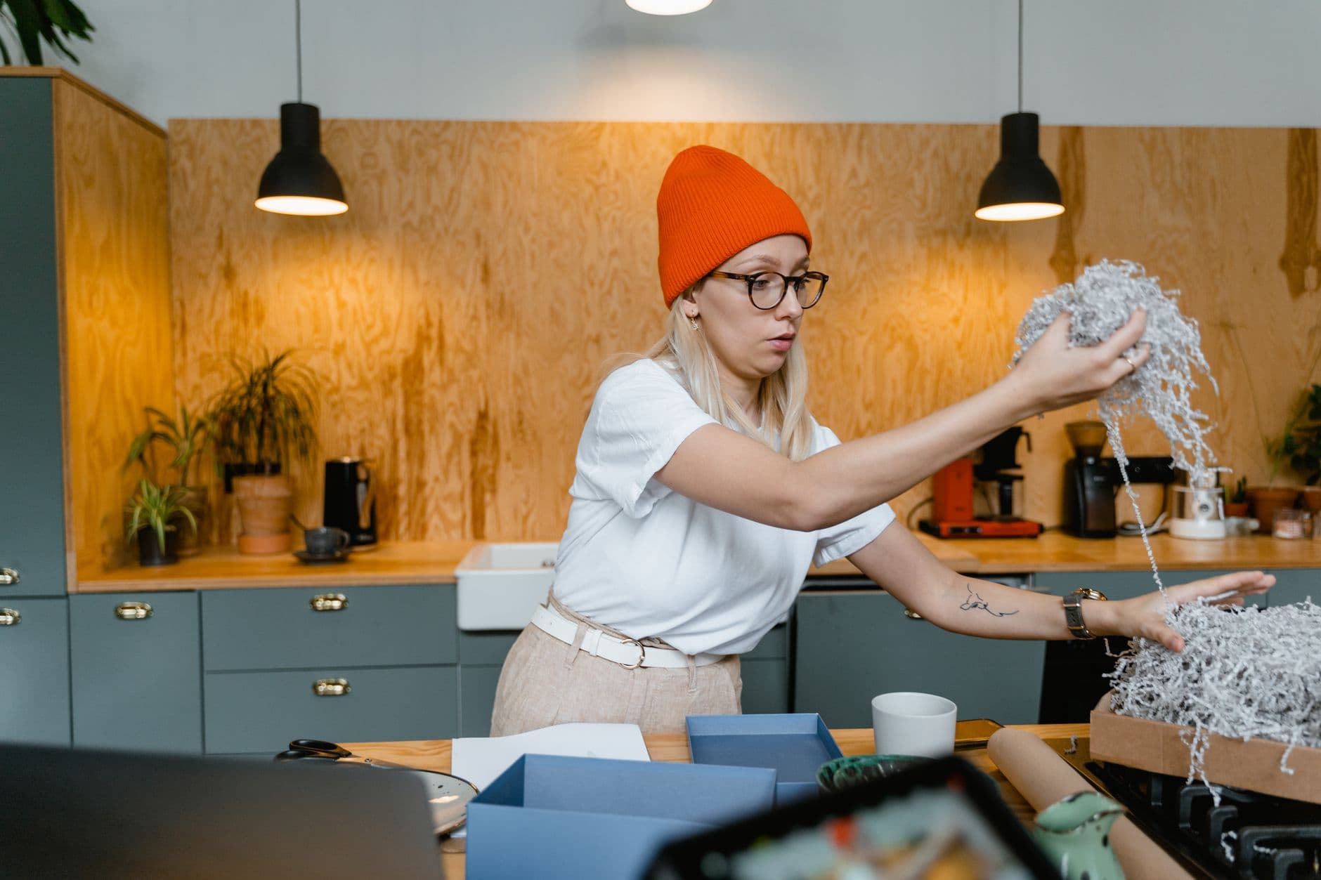 A woman wearing a beanie organizes shredded paper in a stylish kitchen interior.