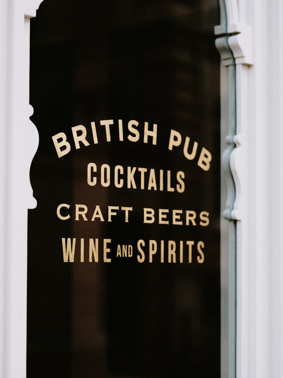 Close-up of a British pub's glass door displaying cocktails, craft beers, wine, and spirits.
