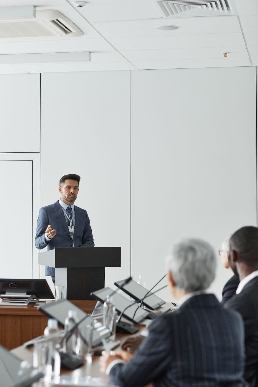 A man in a blue suit giving a presentation at a conference podium indoors.