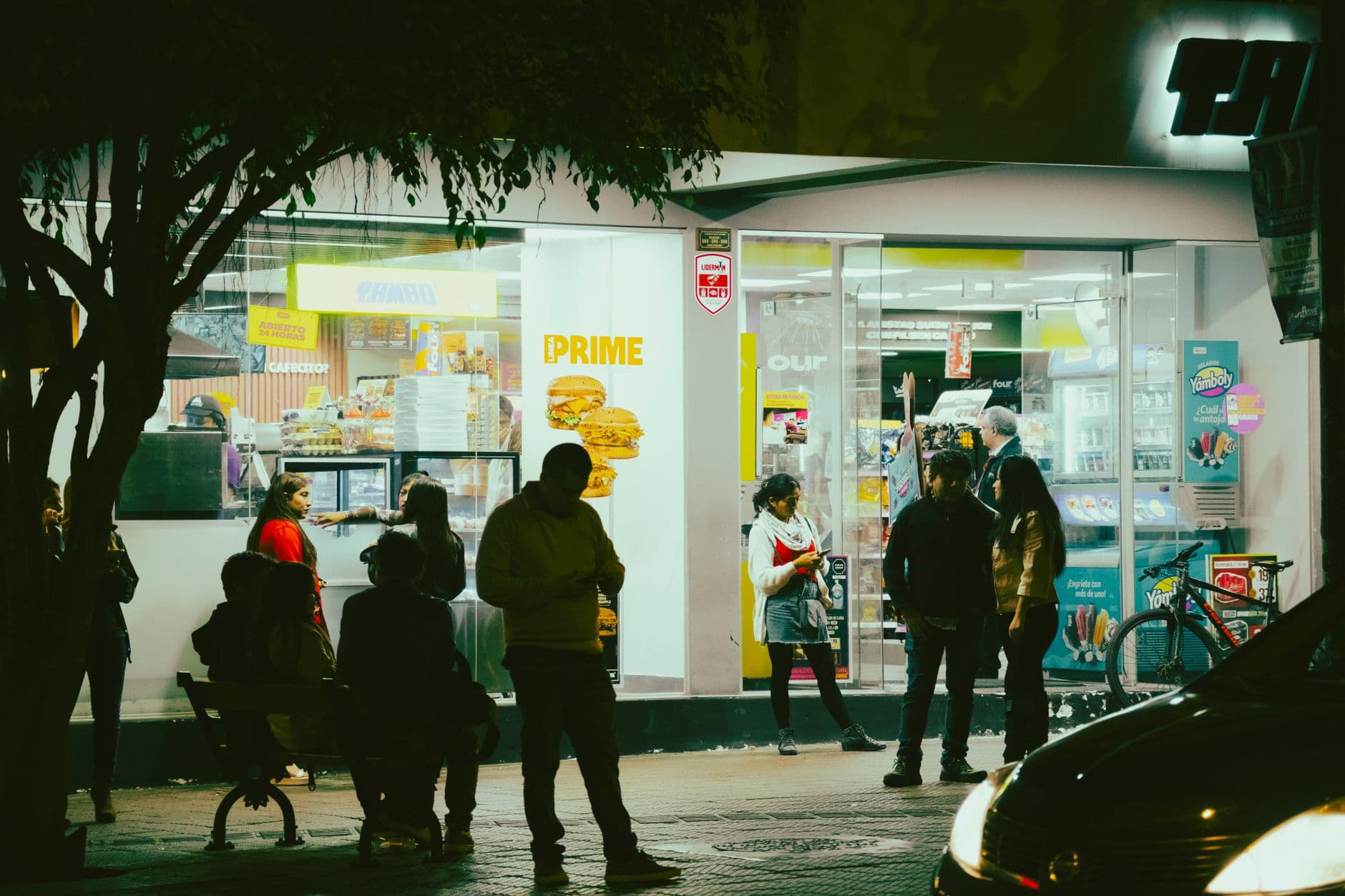 People socializing outside a convenience store at night, capturing urban nightlife atmosphere.