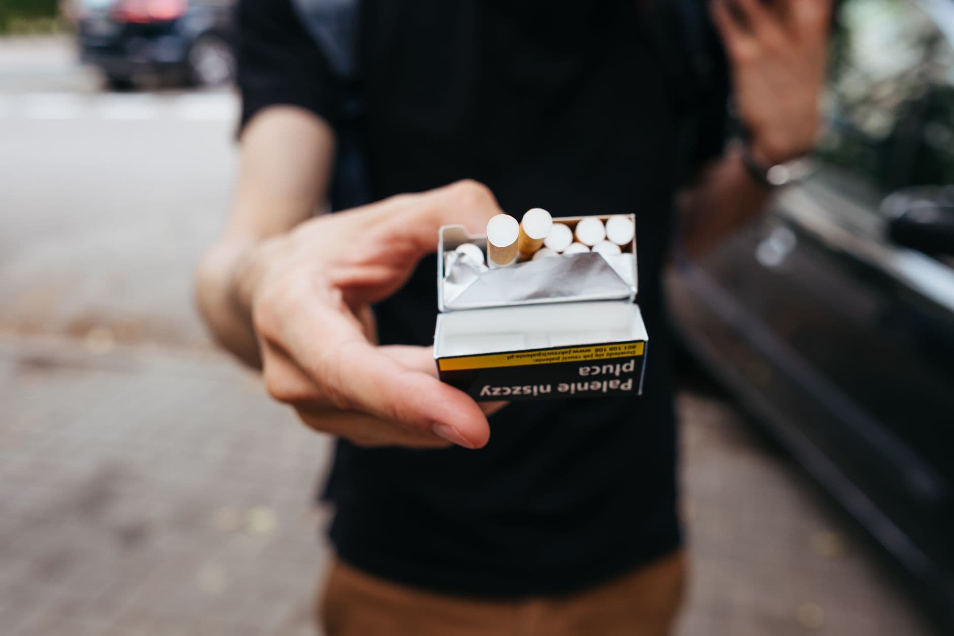 Close-up of a man offering a pack of cigarettes outdoors on a city street.