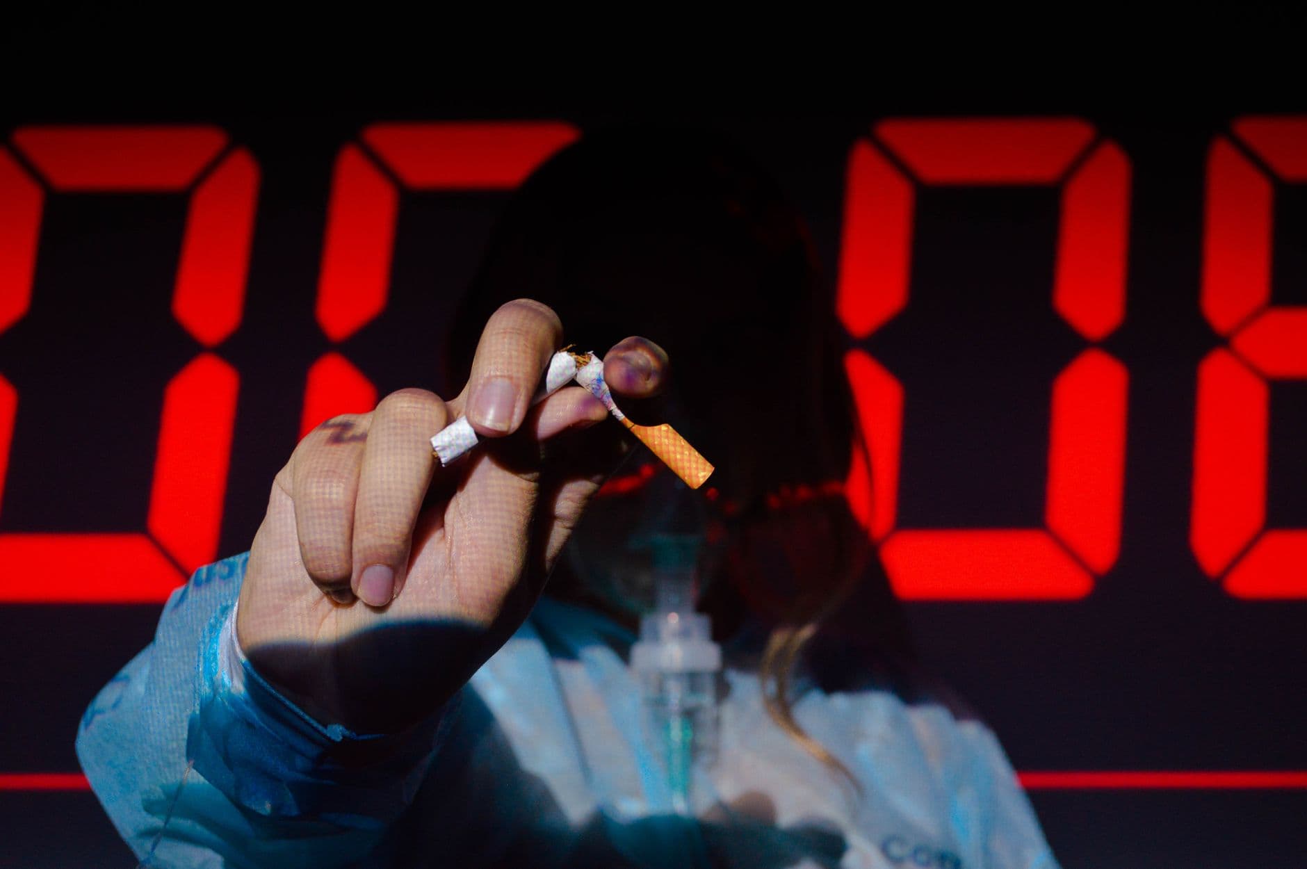 A hand holding a broken cigarette in front of a digital timer, highlighting the urgency of quitting smoking.