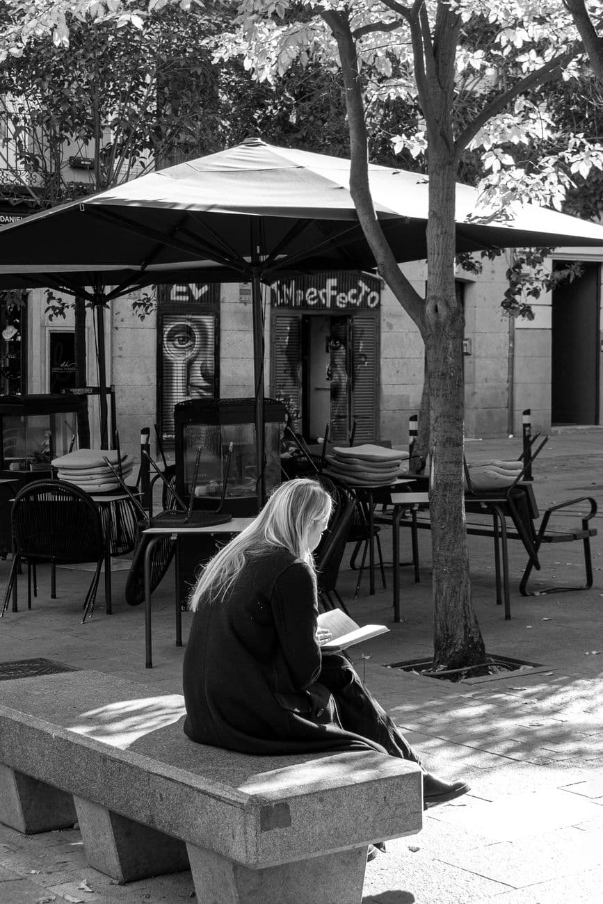 Black and white photo of a woman reading on a bench in a Madrid plaza, Spain.