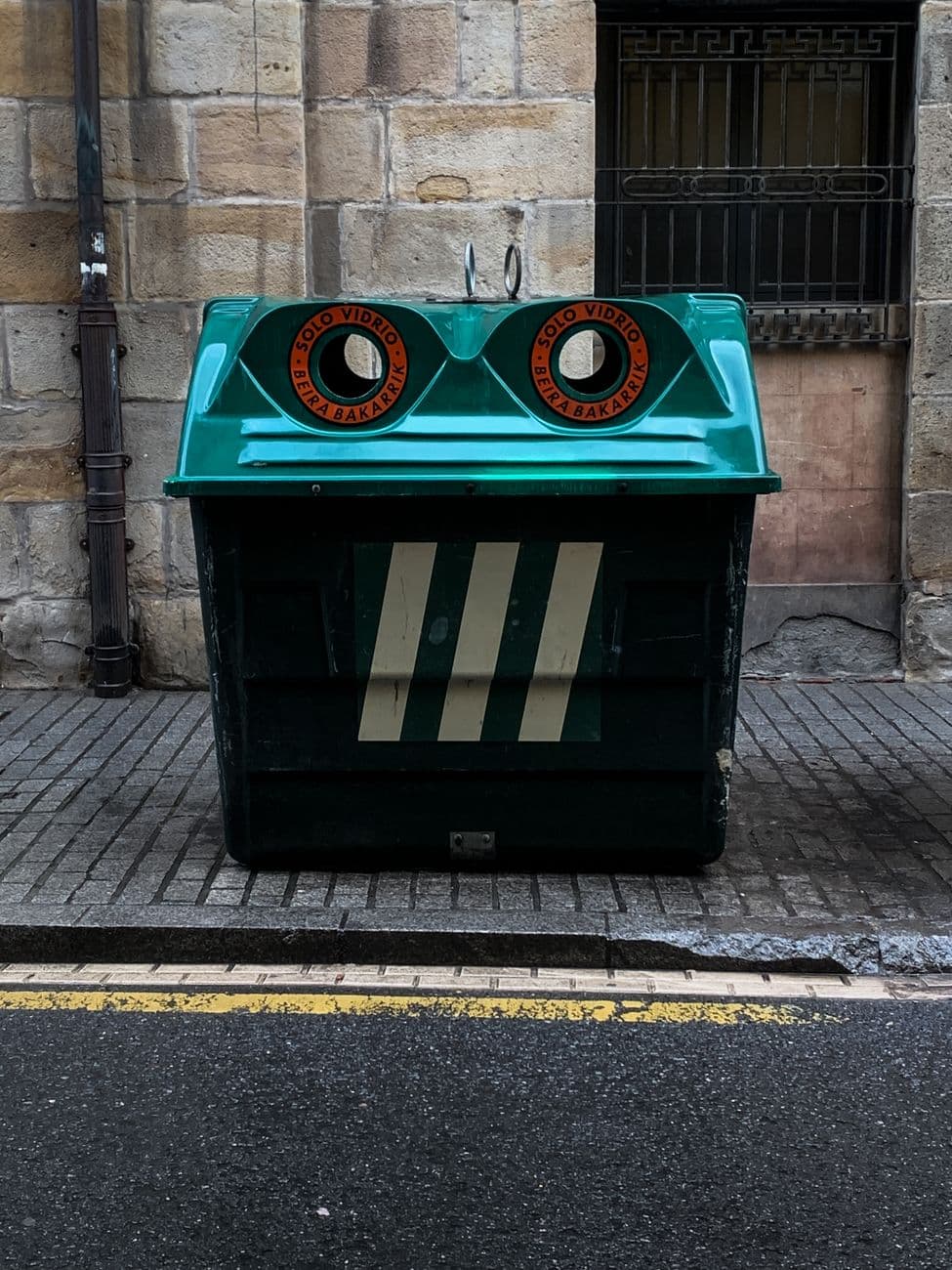 Urban street scene featuring a unique garbage bin with a face-like appearance in Bilbao, Spain.