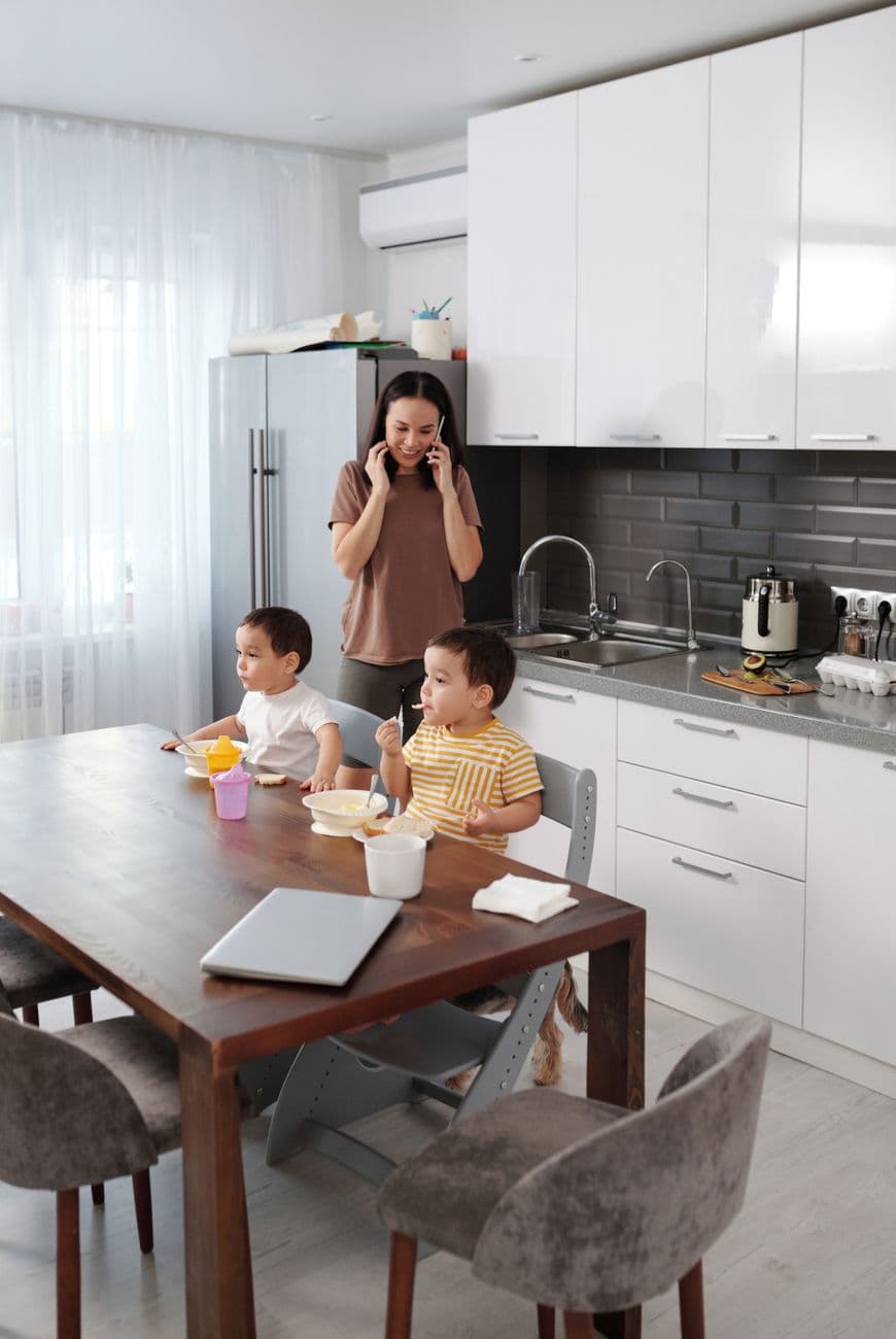 Mother multitasking with sons eating breakfast in a modern kitchen.