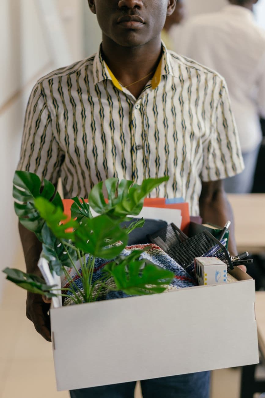 A man carrying a box of office belongings including plants and documents.