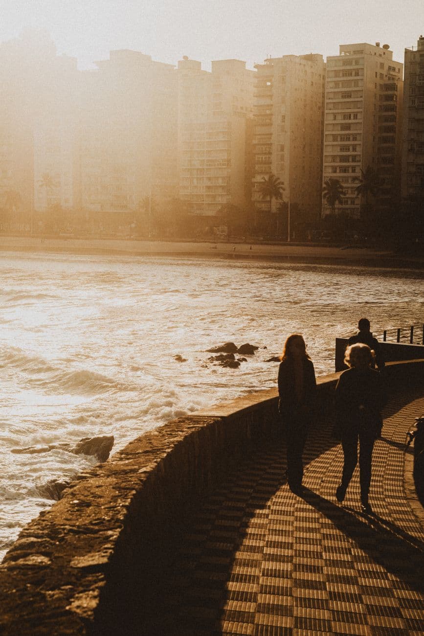 Silhouetted people walking by the sea during sunset in an urban setting.