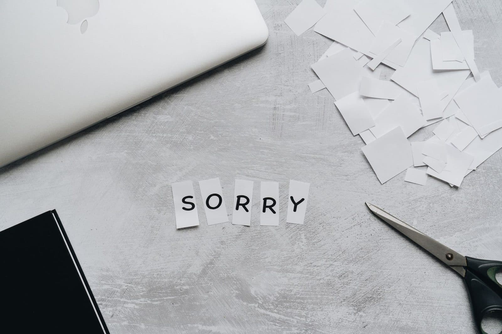 Top view of a desk with cut-out letters spelling 'sorry', scissors, and a laptop.