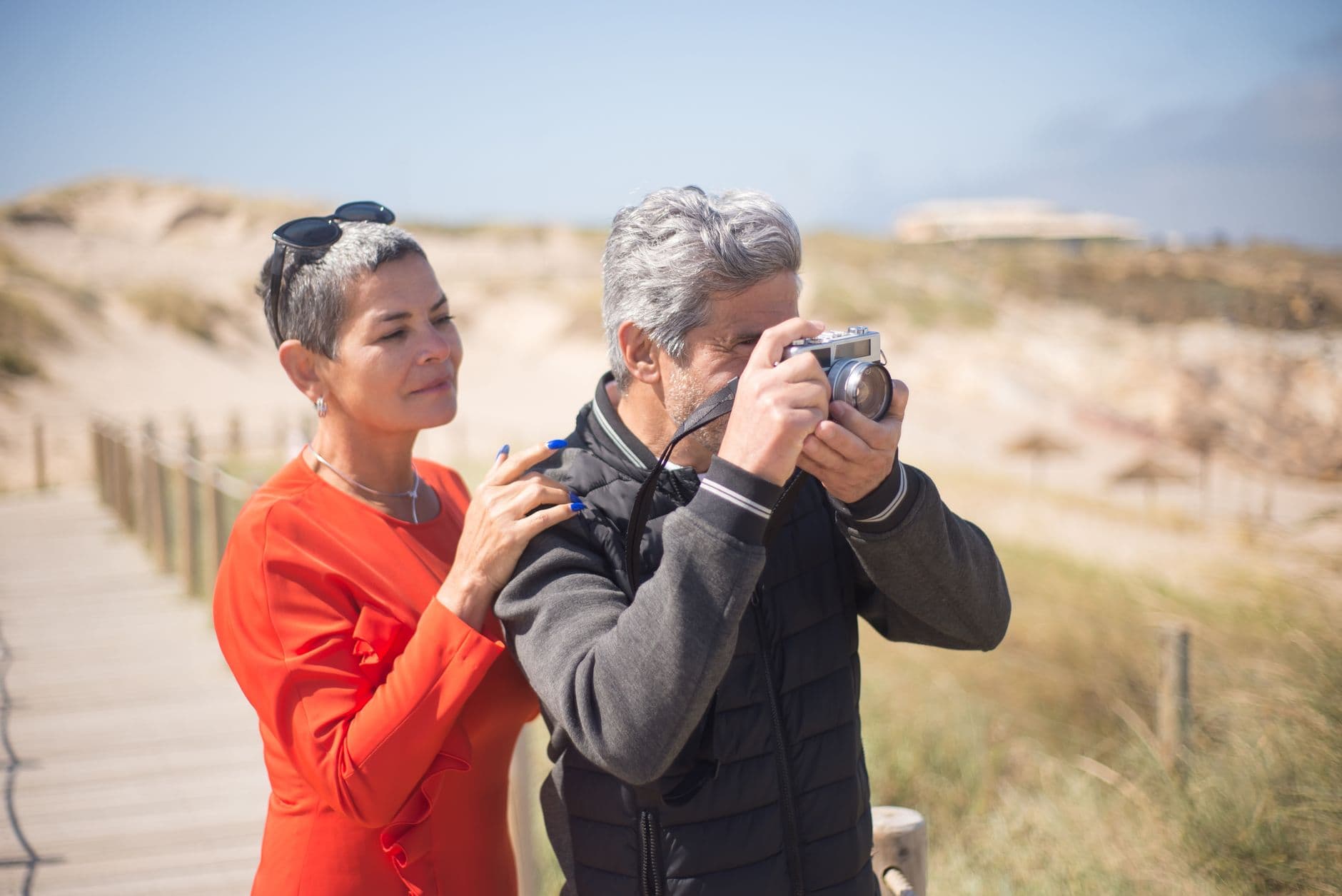 A senior couple exploring a beach boardwalk with a vintage camera in Portugal.