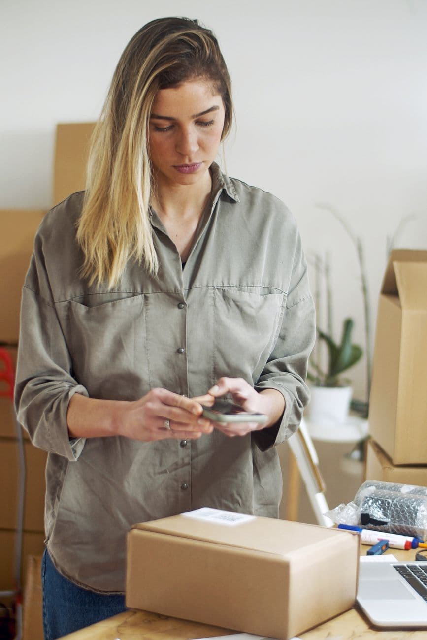 Woman capturing images of packages with her phone in a home office, ready for shipping.