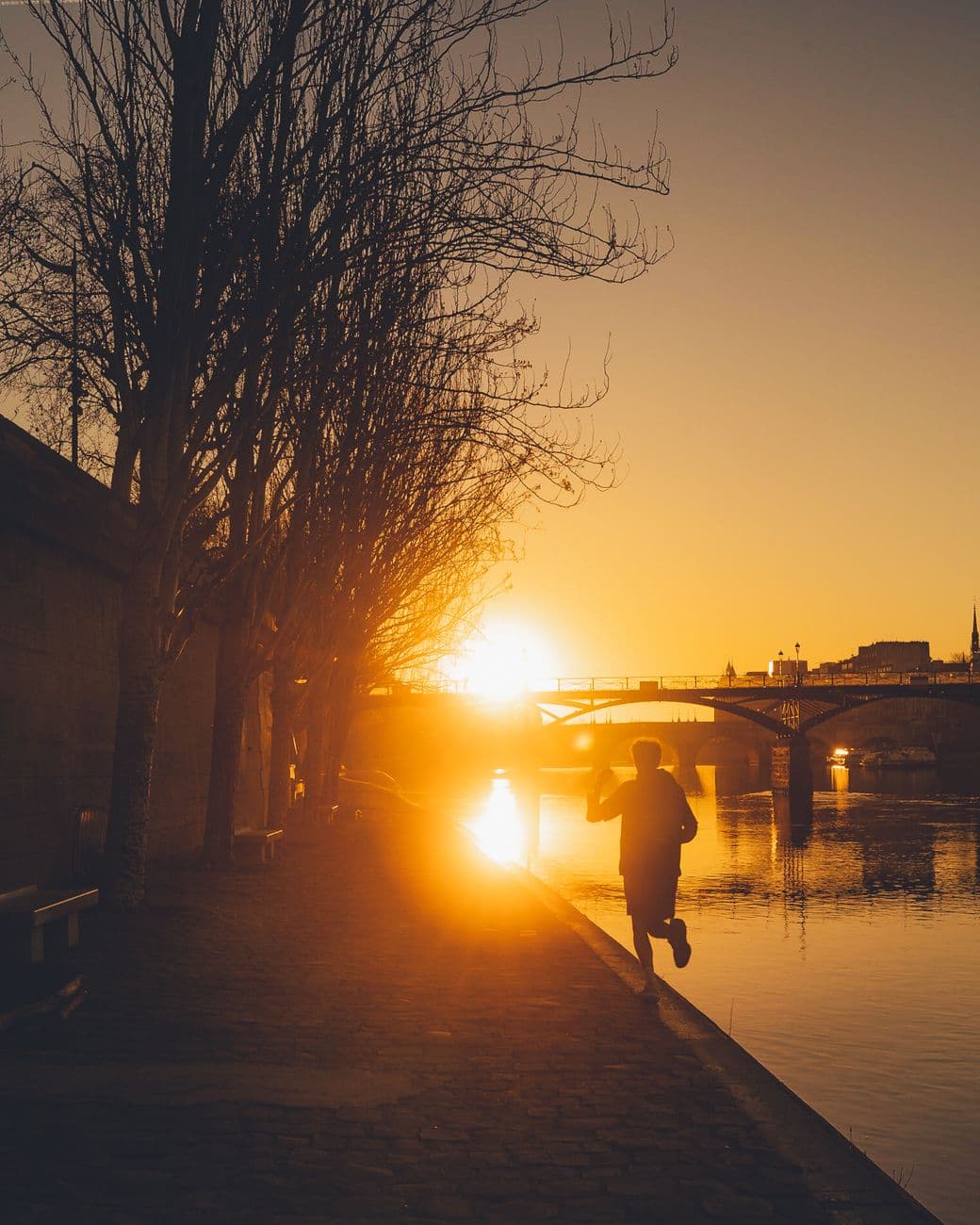 Silhouette of a man jogging along the Seine River in Paris during a vibrant sunset.