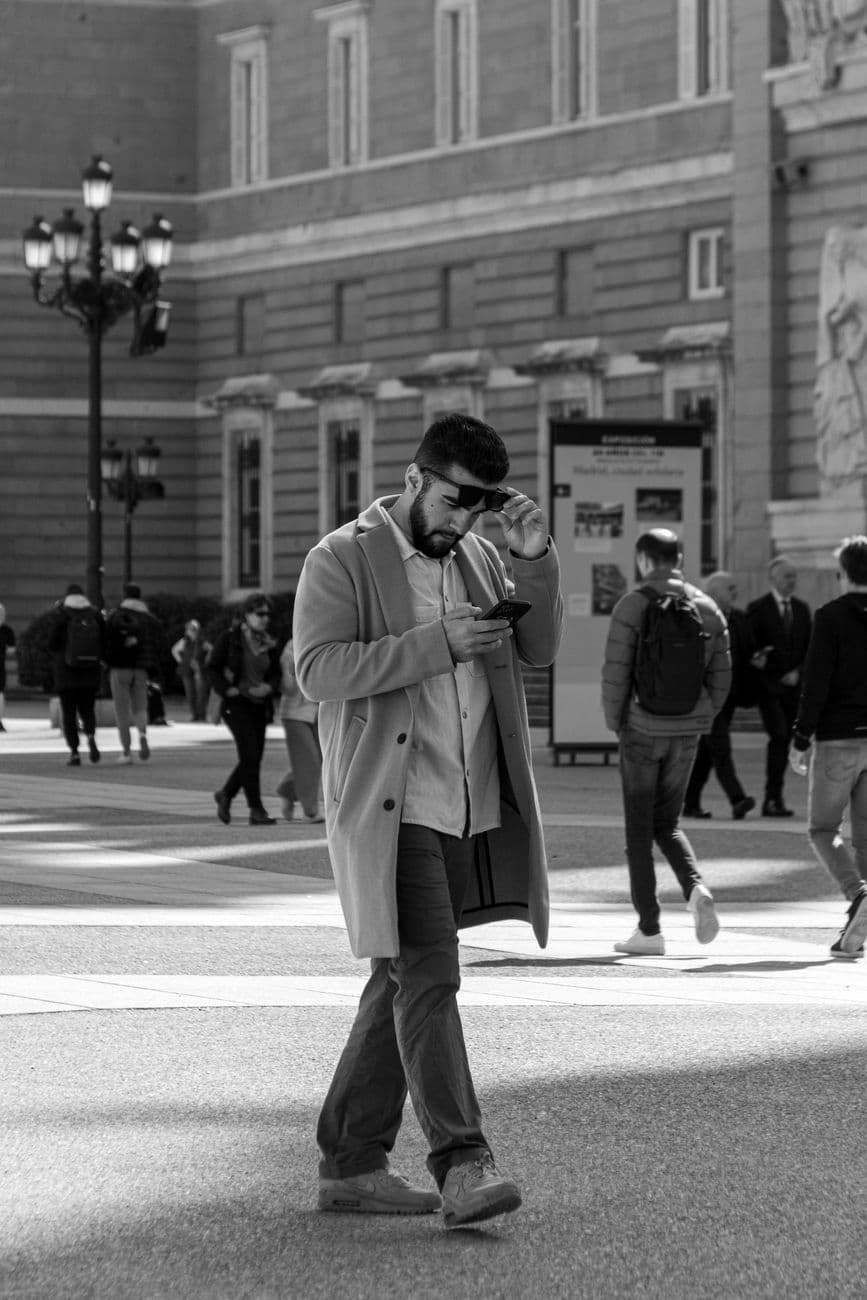 Black and white photo of a man walking in a busy Madrid street while using his phone.