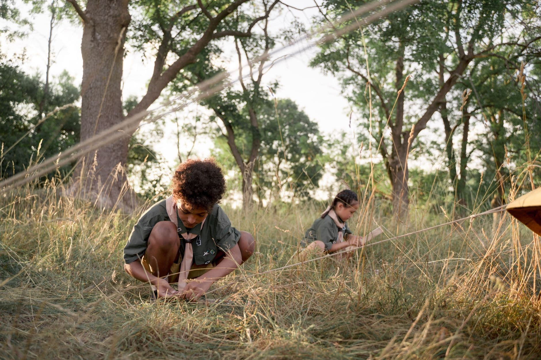 Two children setting up a tent in a sunlit forest, engaging in a camping adventure.