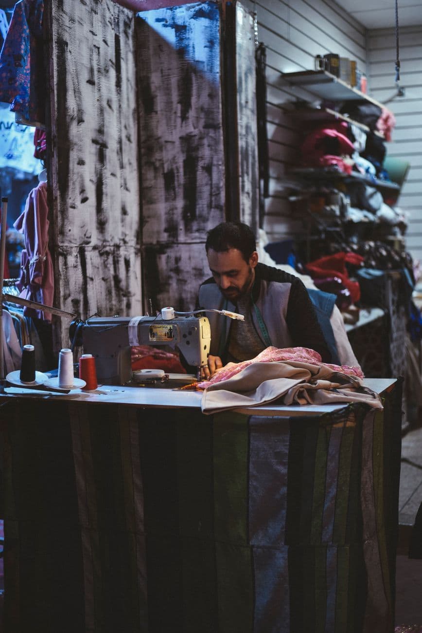 Skilled tailor sewing garments on a machine in a cozy Agadir fabric shop.