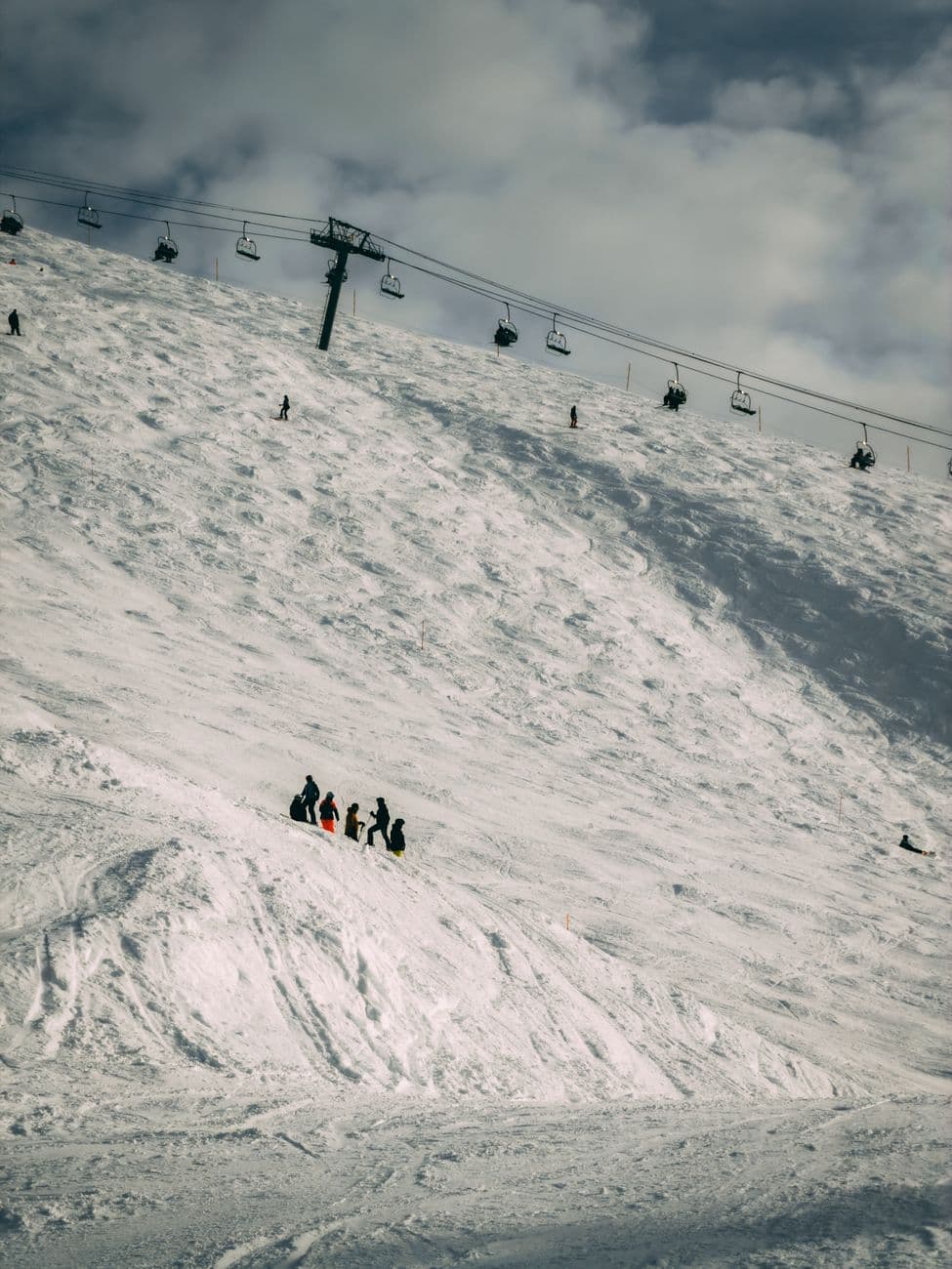 A group of skiers navigate a snowy slope below a chairlift under cloudy skies.